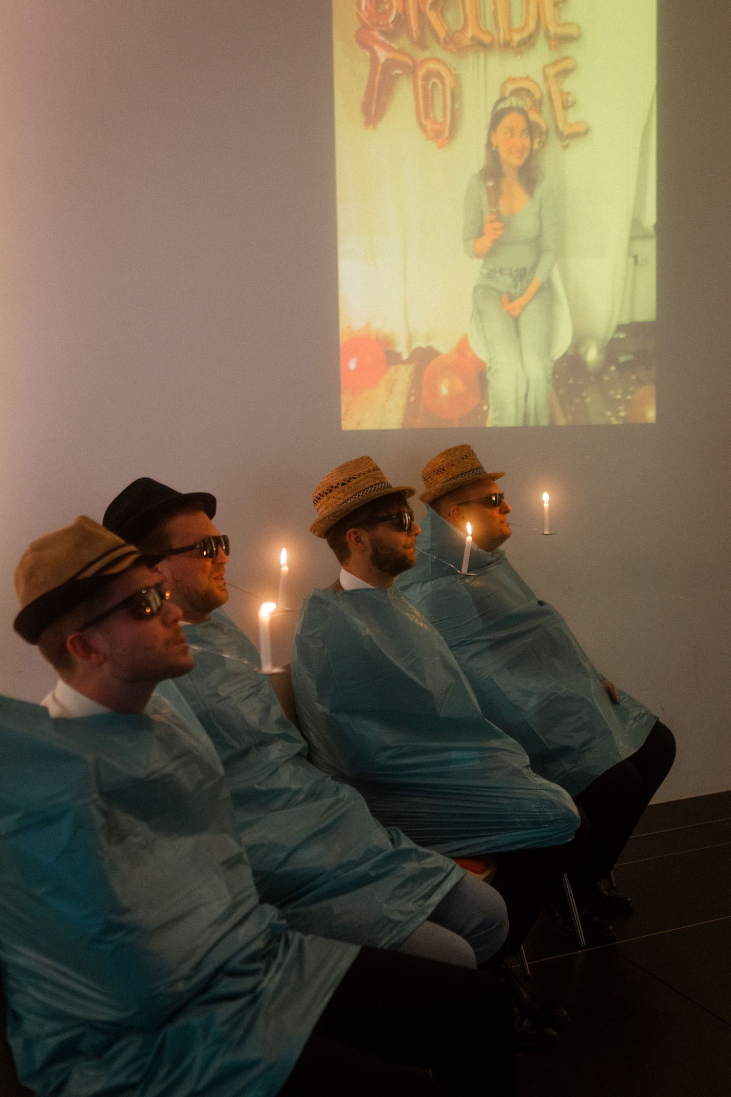 People in matching blue outfits and hats watch a projection screen with candles lit.
