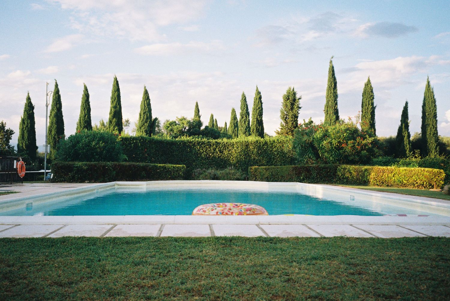 Long swimming pool surrounded by cypress trees and manicured landscaping in Tuscany.