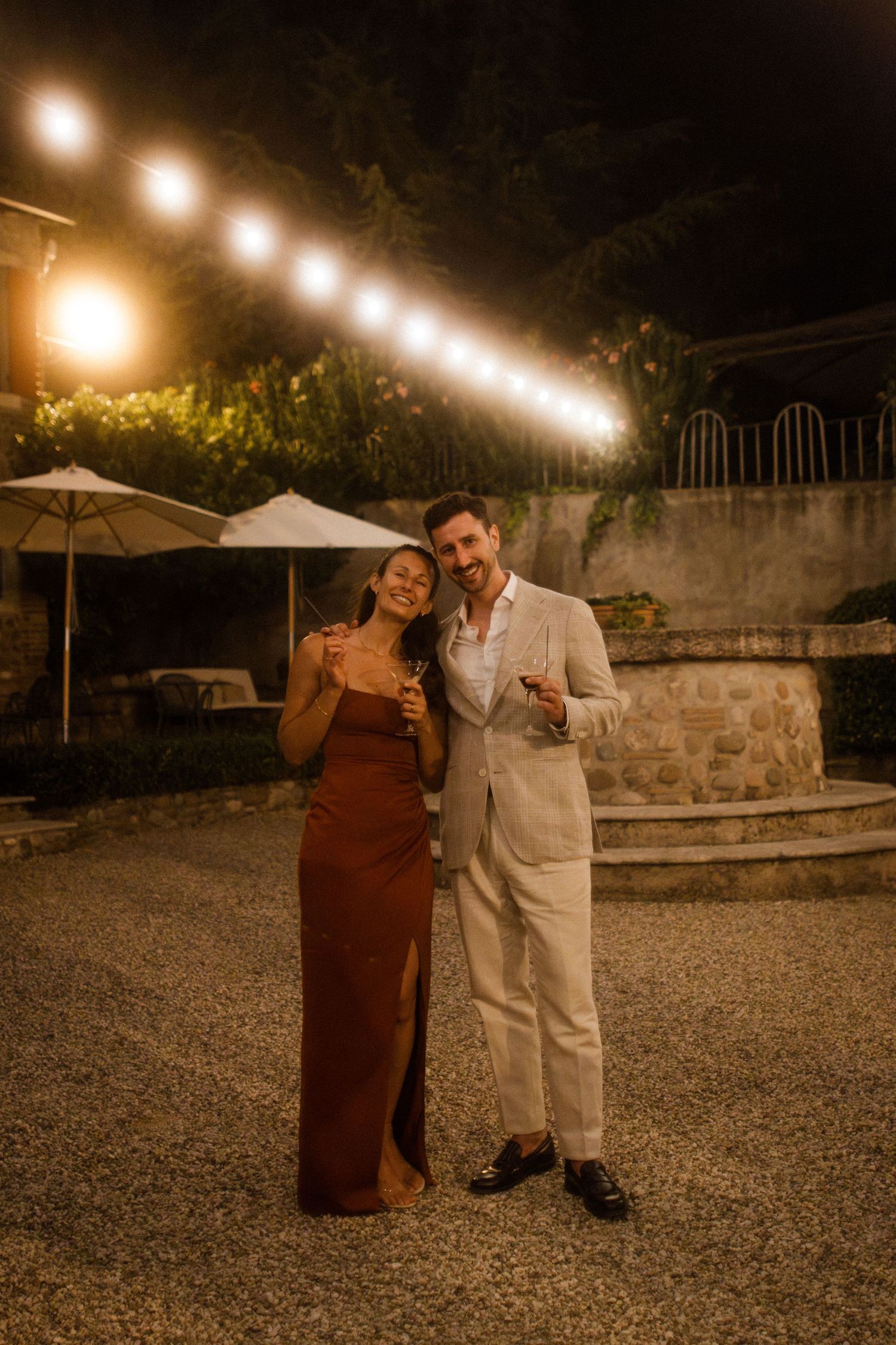 A couple poses together at an outdoor evening event with string lights overhead.