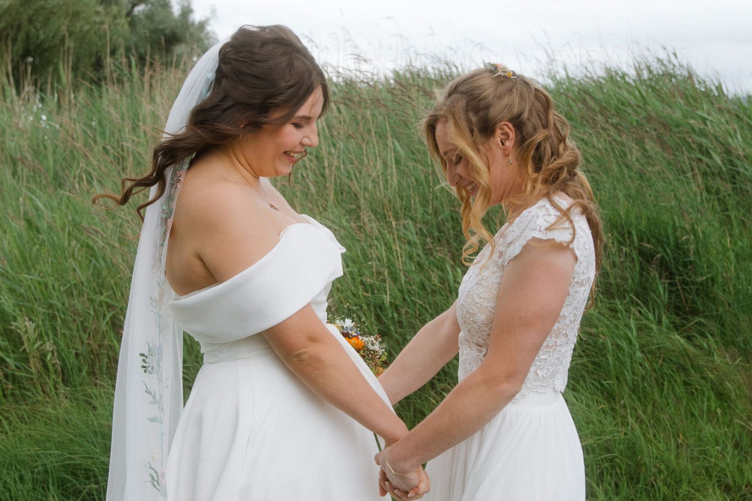 Two people in white wedding attire share intimate moments in a field of tall grass.