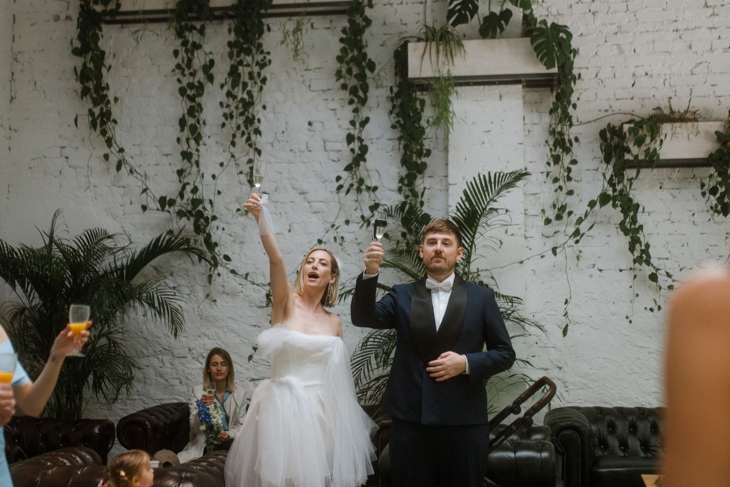 Wedding celebration sequence against a white brick wall decorated with hanging greenery.