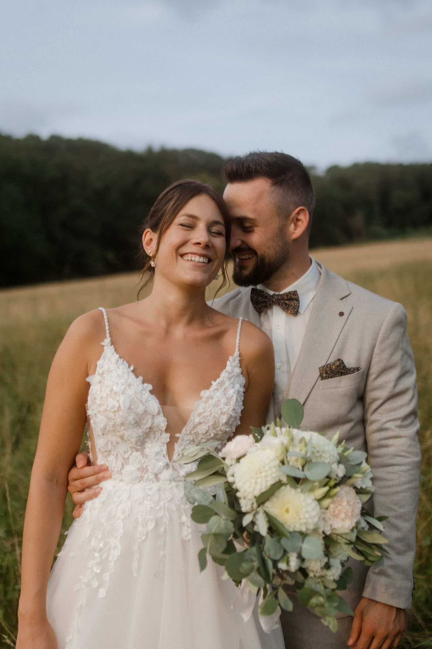 Couple in wedding attire sharing an intimate moment in a sunny meadow.