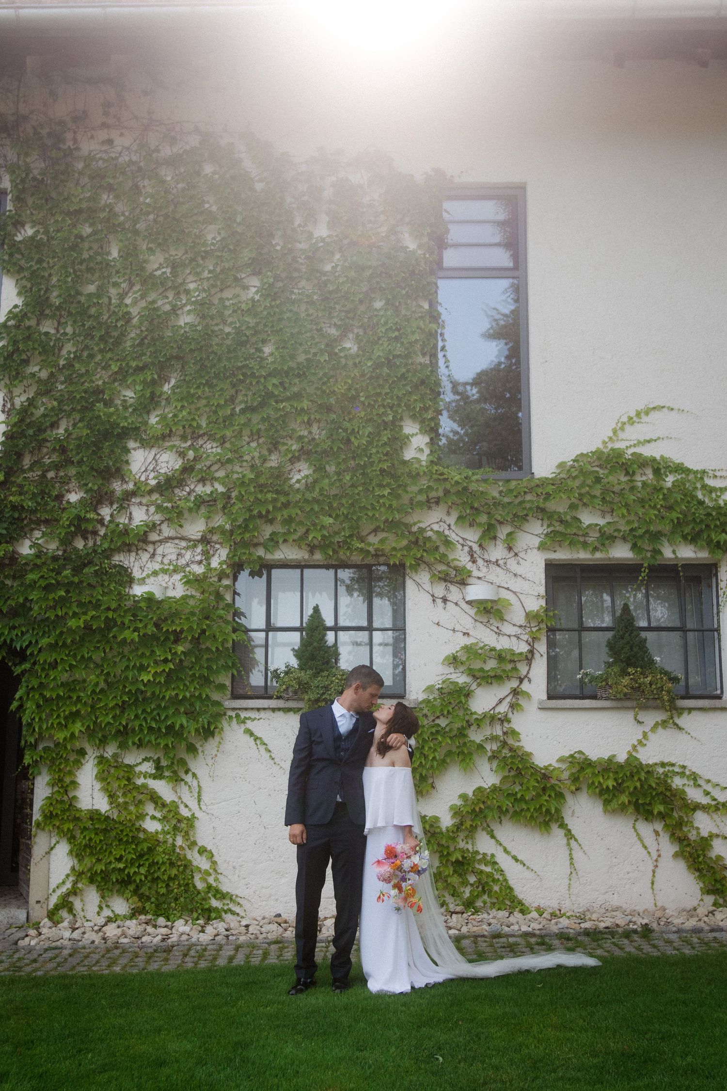 A couple poses against an ivy-covered white building for their wedding photos.
