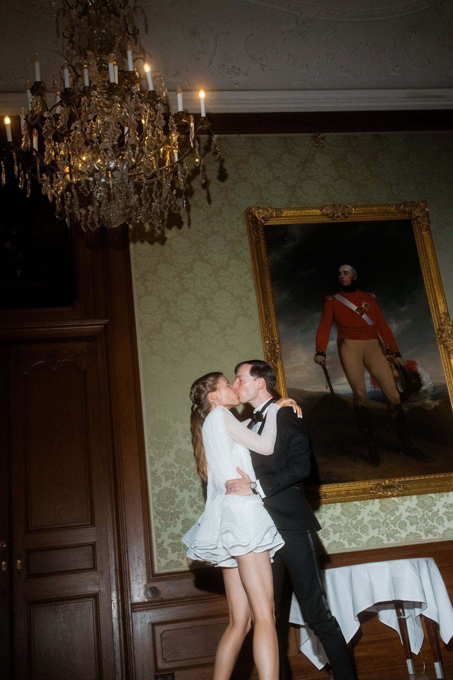 Couple sharing a romantic dance moment beneath a chandelier and classical portrait.