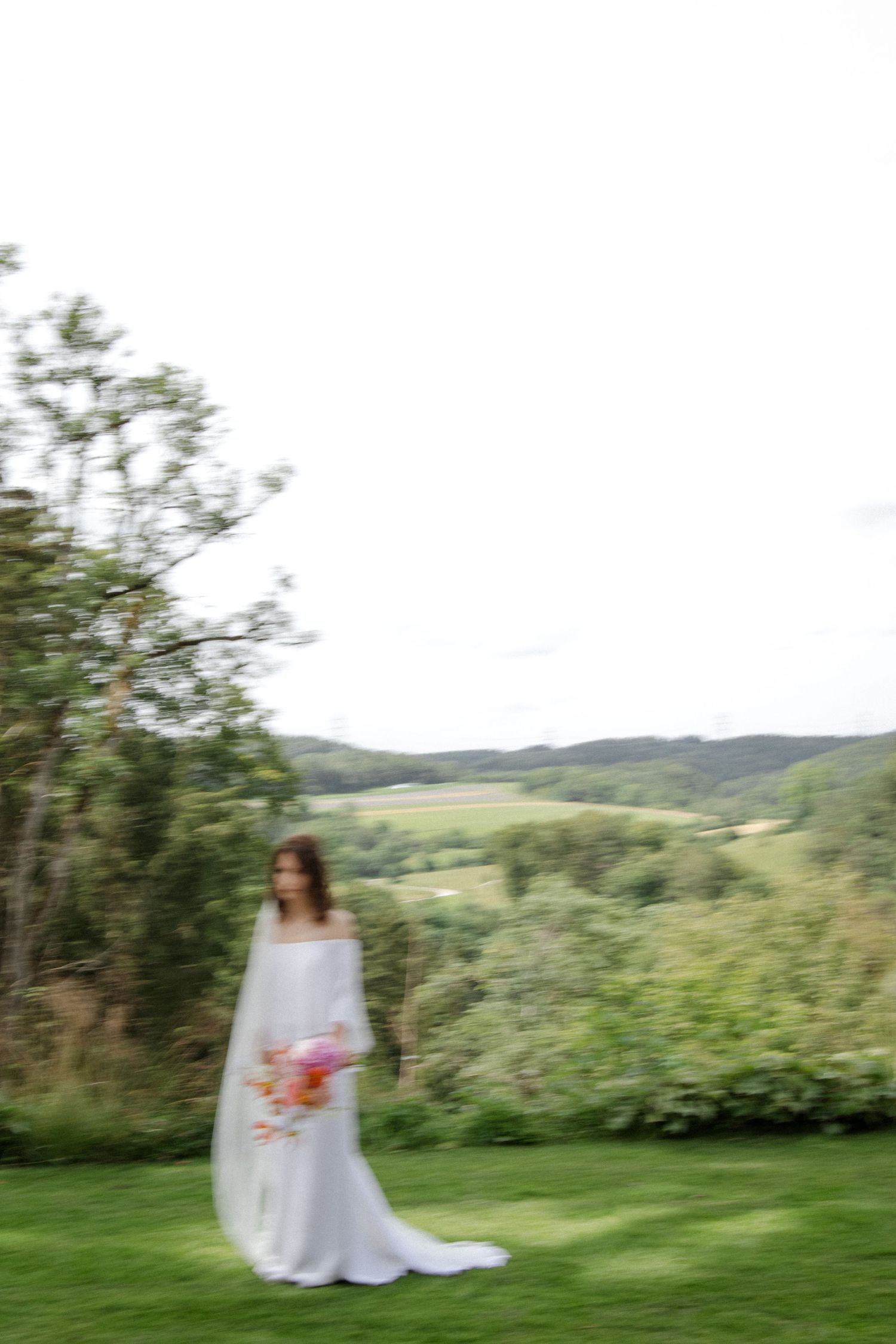 Artistic motion blur photograph of a bride in white holding a coral bouquet on a green lawn.