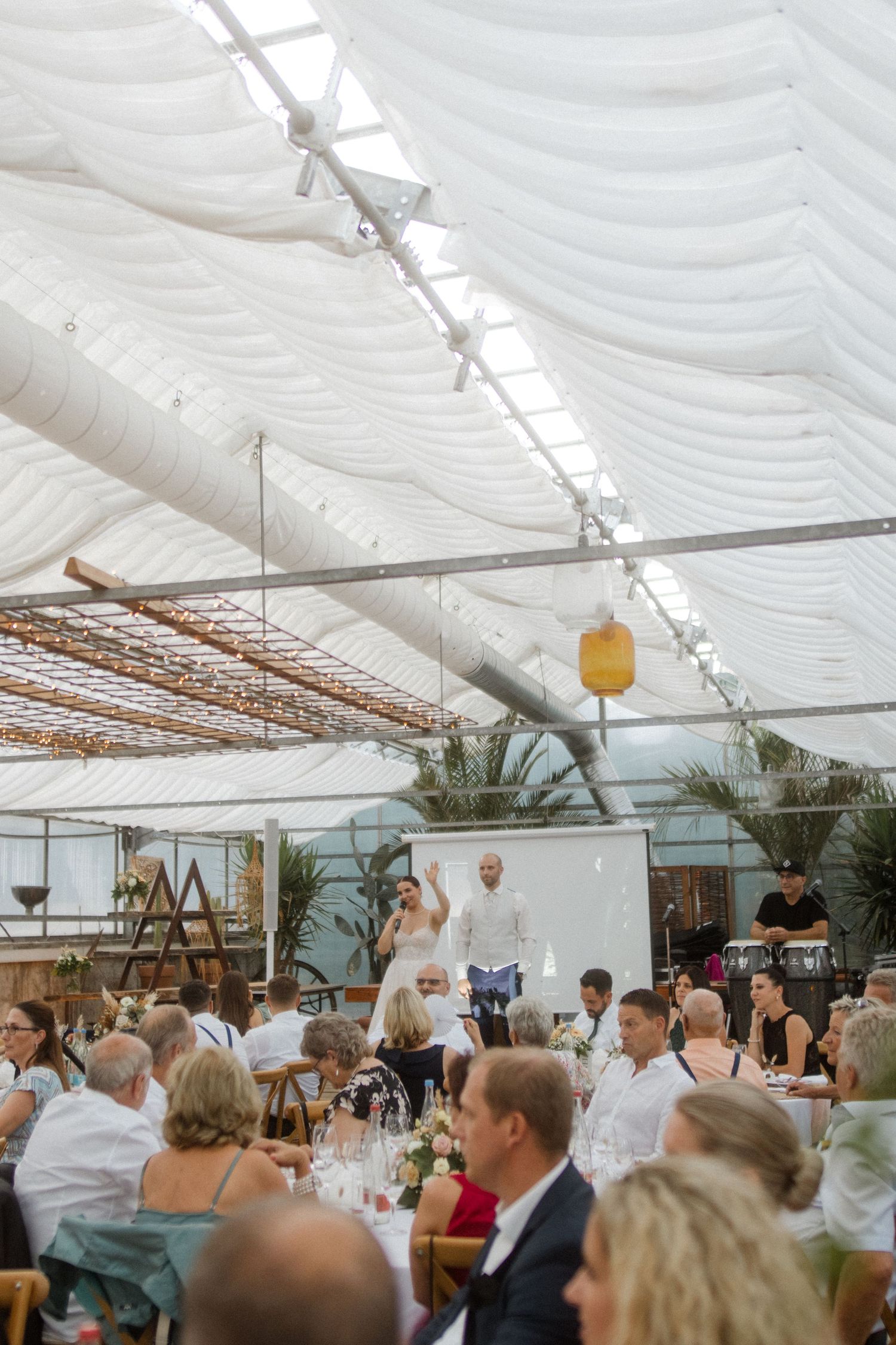 Wedding reception venue with white tent covering and guests seated at long tables.