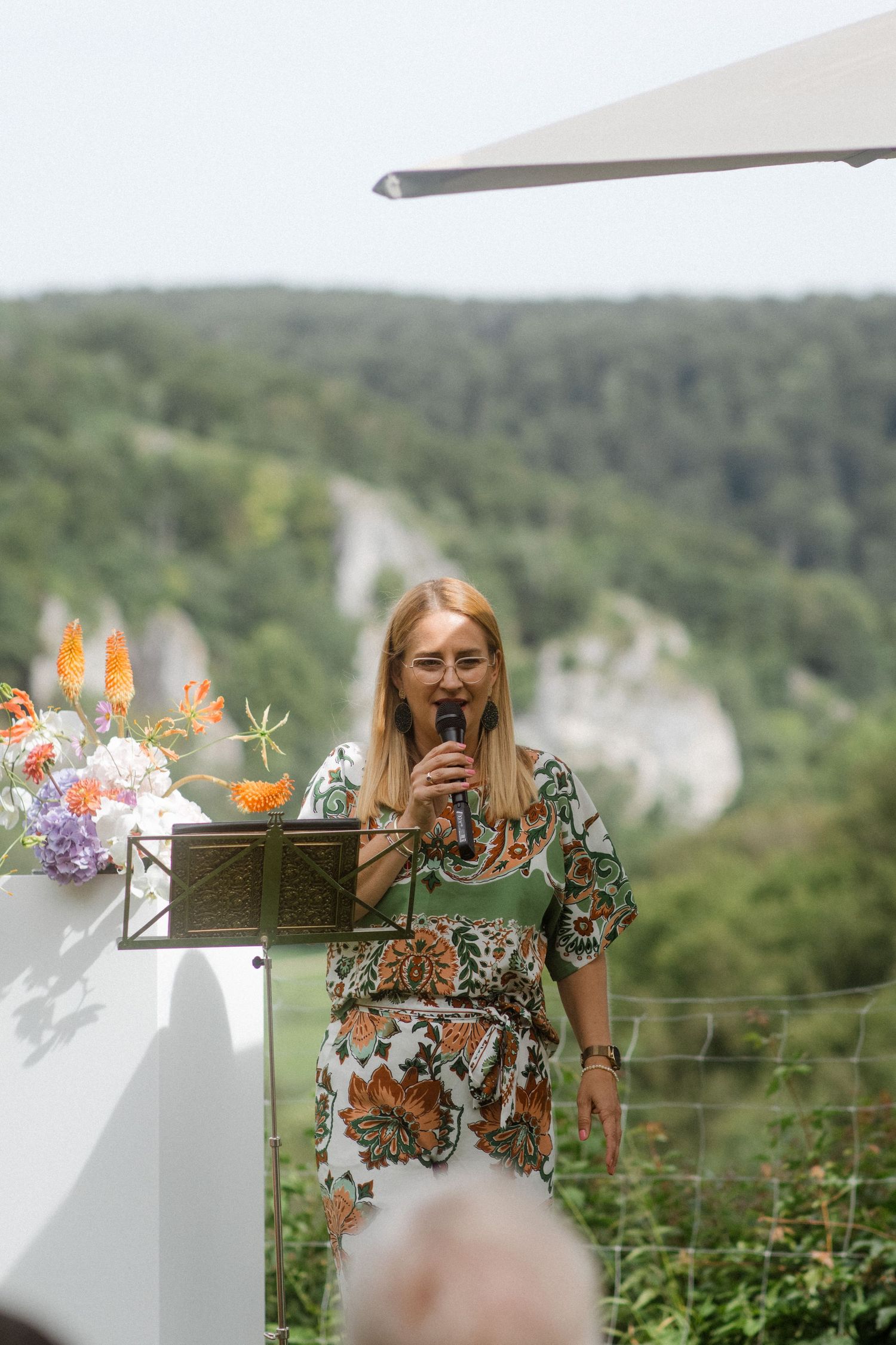 Speaker at outdoor wedding podium with scenic mountain backdrop.