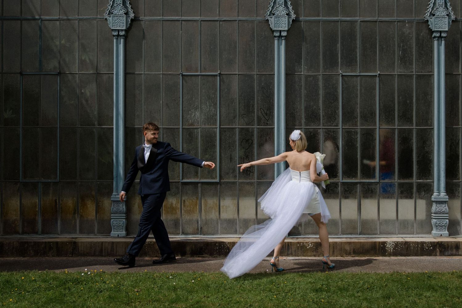 Playful wedding photo with couple creating dynamic poses against architectural backdrop.