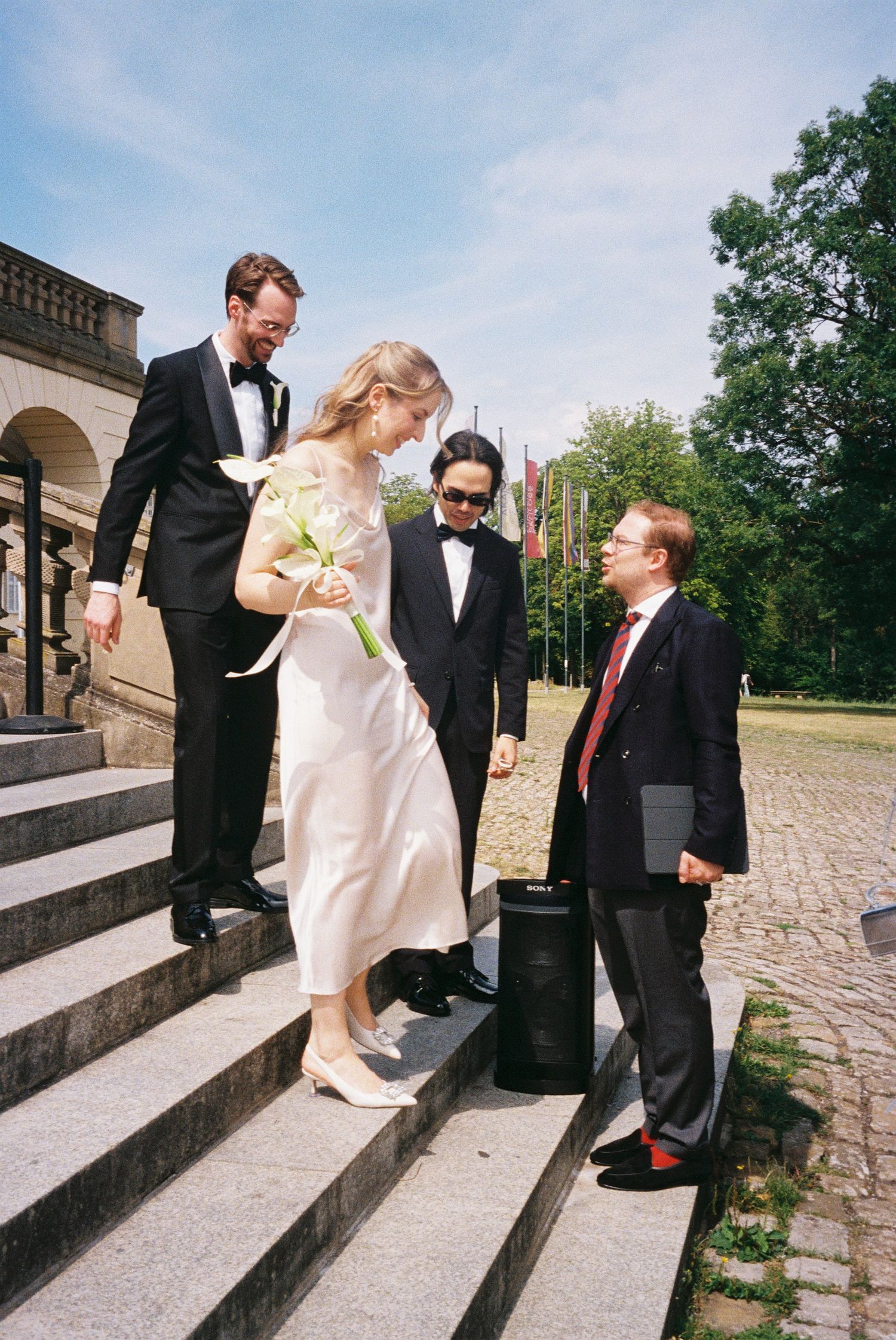 Wedding party members in formal attire standing on stone steps outside a building.