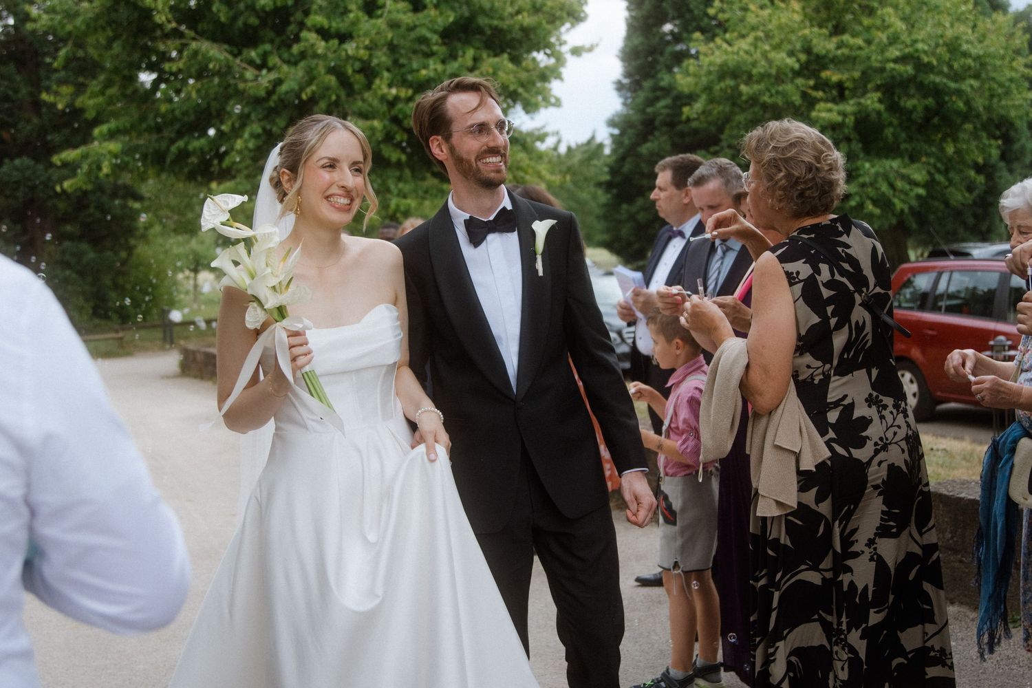 Joyful wedding celebration with guests cheering along a tree-lined path.