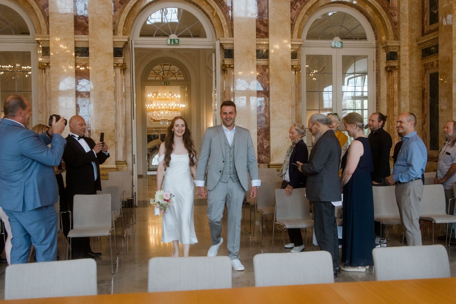 A grand historic building interior with arched columns and elegant architectural details hosts a wedding gathering.