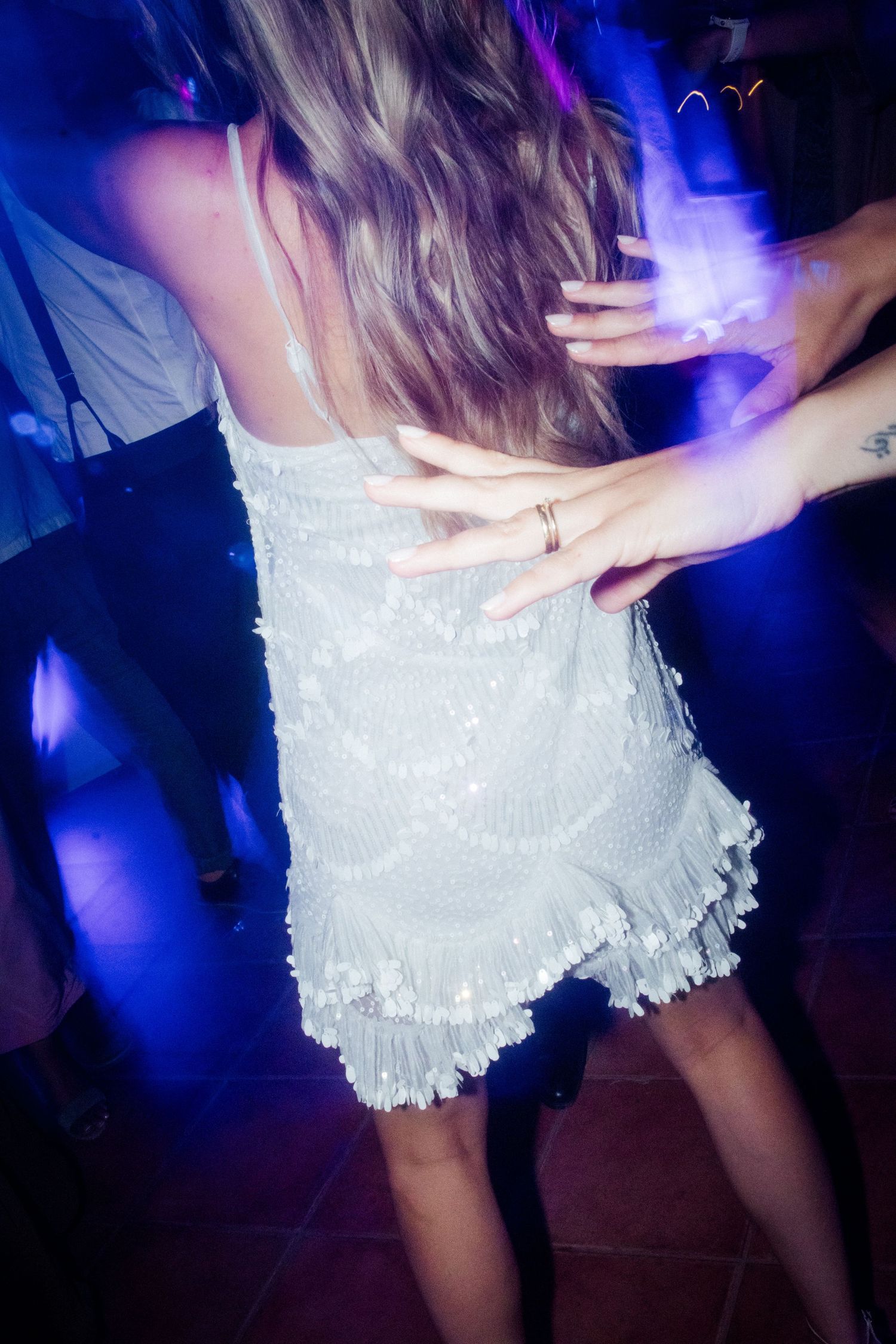 White sequined dress twirls on dance floor under blue lighting at wedding reception.