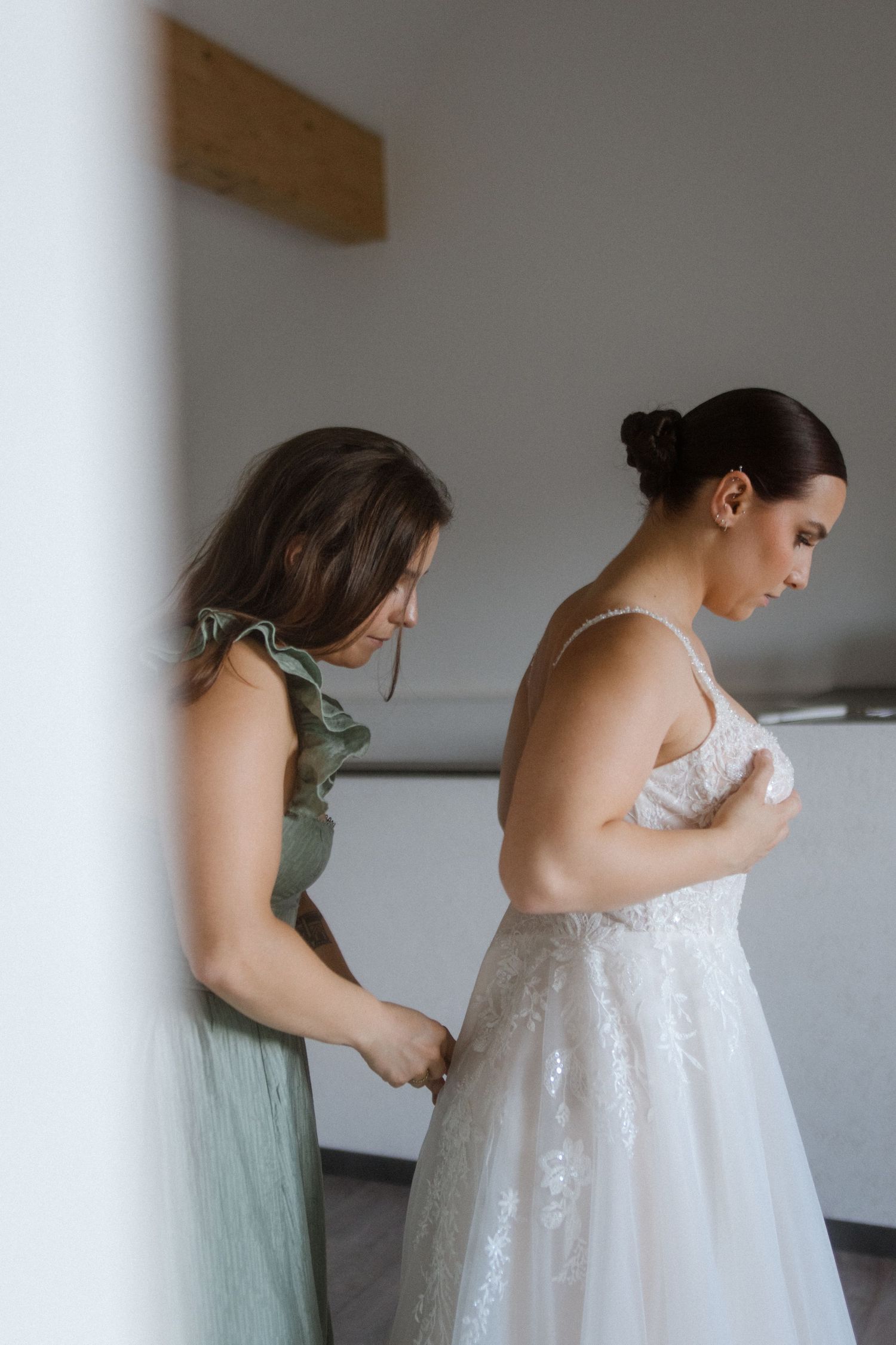 Bridesmaids in sage green dresses helping with wedding dress preparations.