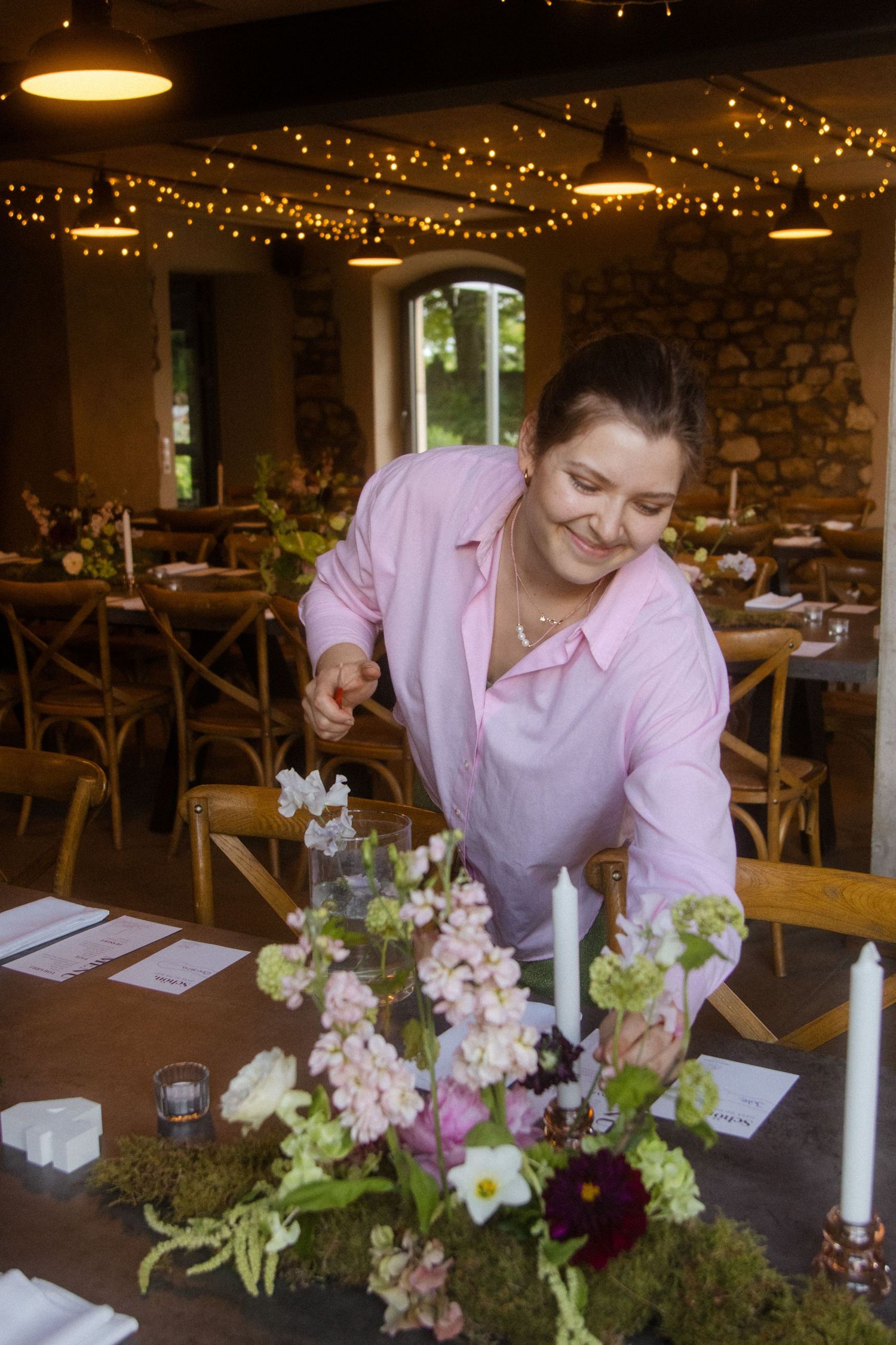 Person arranging flowers on a table with string lights in the background.