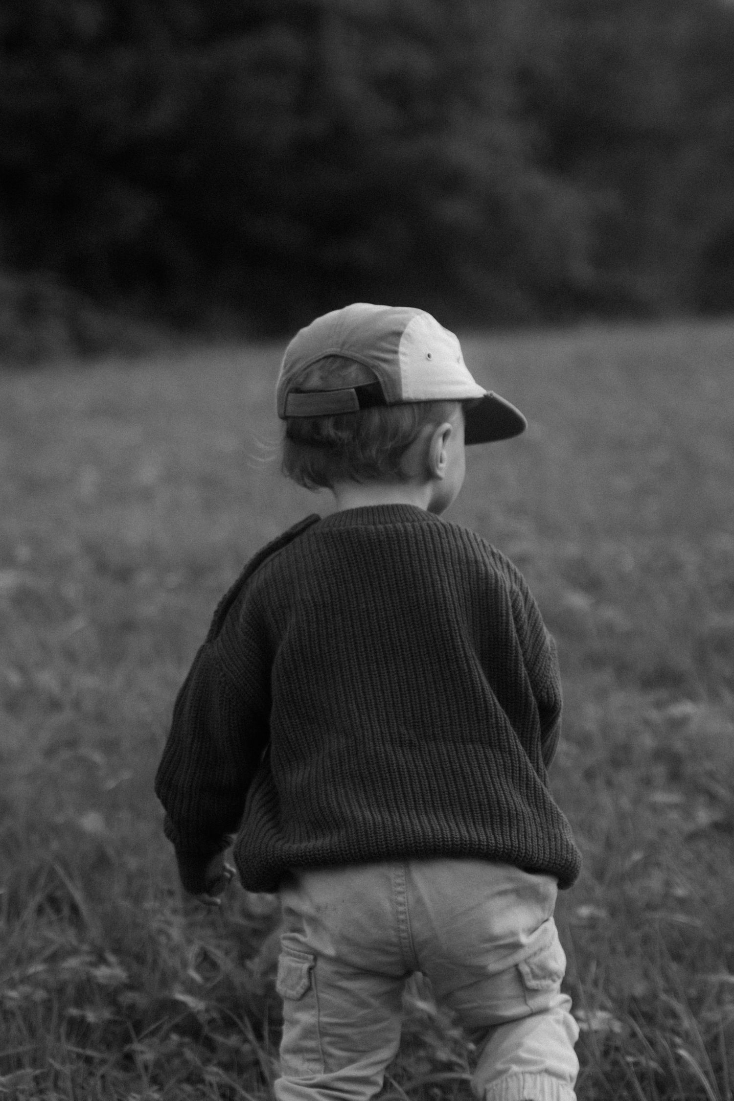 Black and white image of a small child walking through tall grass.