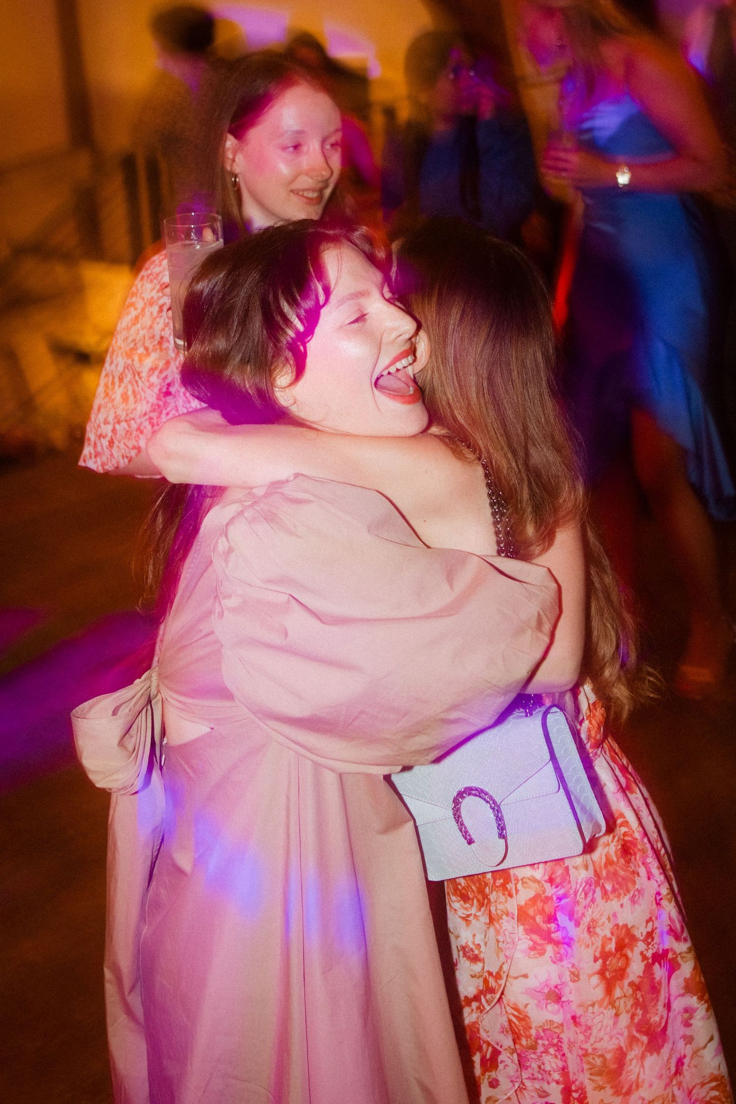 Wedding guests sharing joyful hugs on the dance floor under colorful party lights.