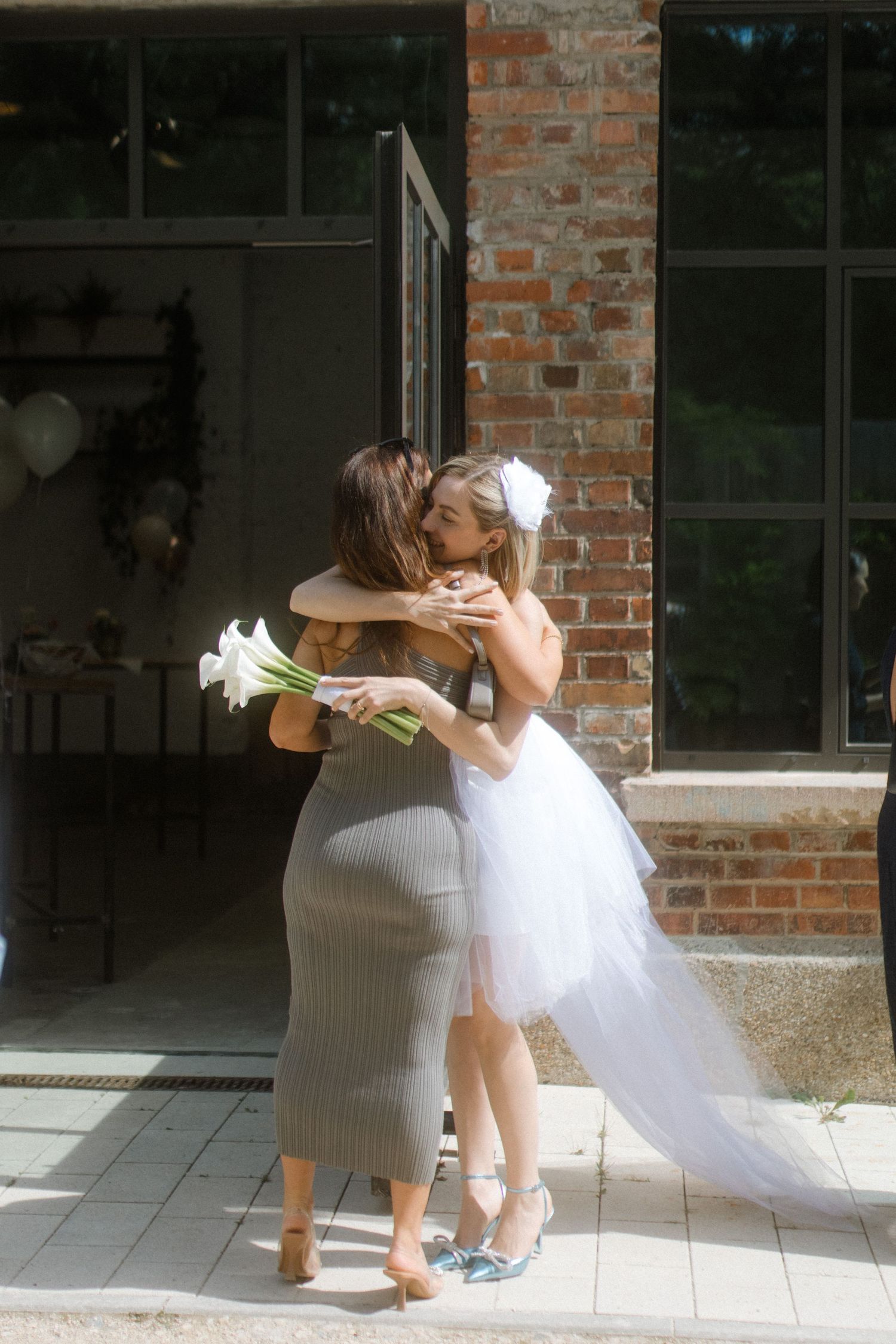 Two people embrace in an emotional moment, with one wearing a flowing white dress holding calla lilies.