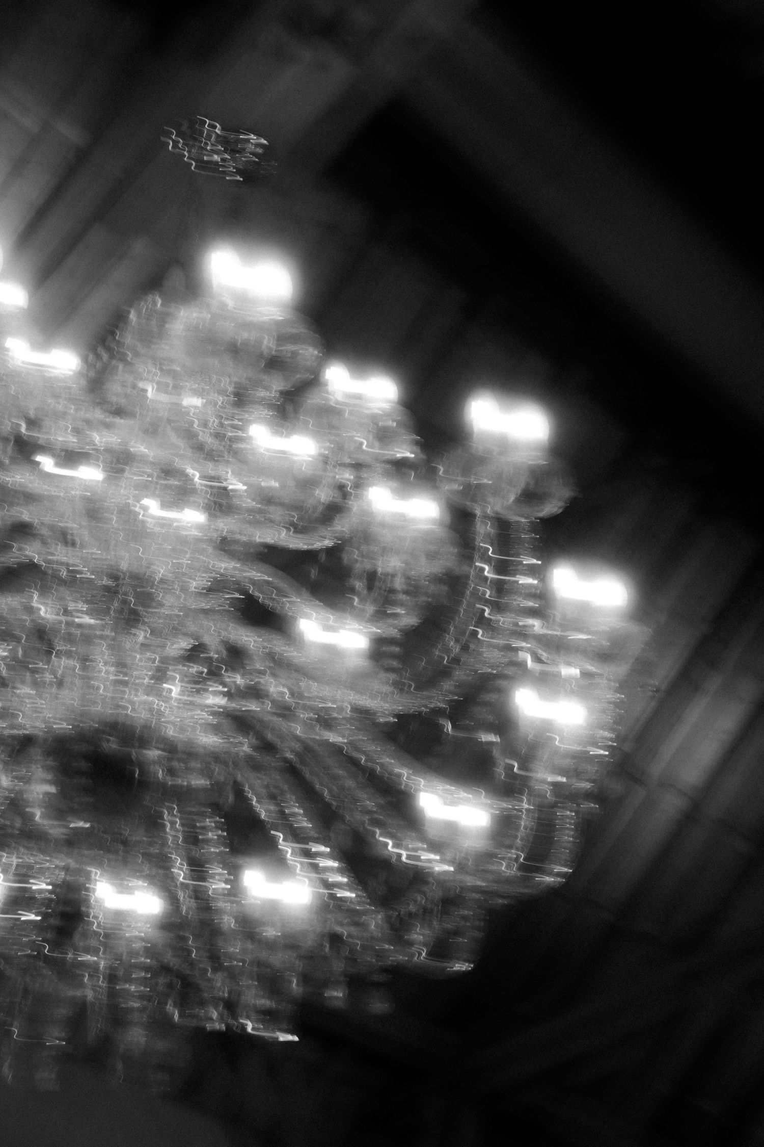 Black and white artistic photo of an ornate crystal chandelier glowing in the darkness.