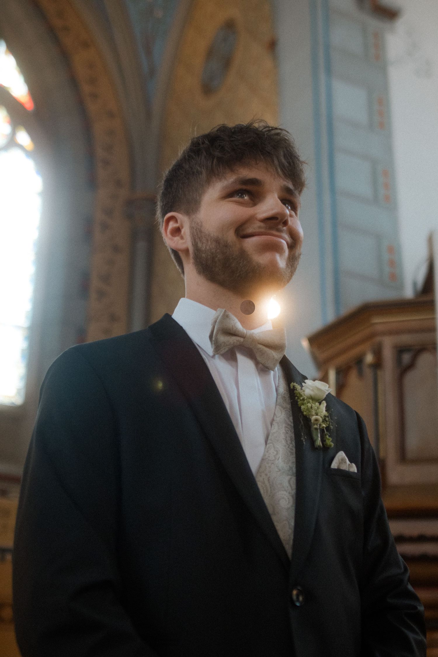 Groom in formal attire smiling inside church with dramatic lighting and architectural details.