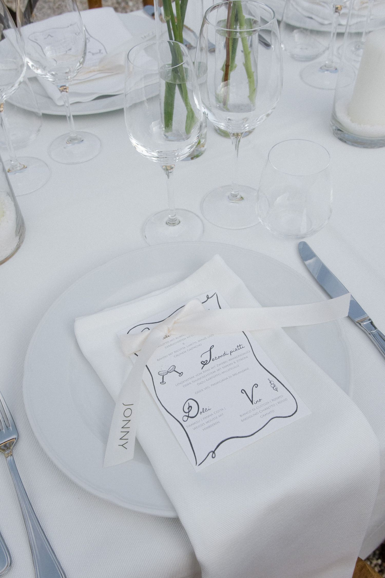 Wedding table settings with white linens, wine glasses, and handwritten name cards.