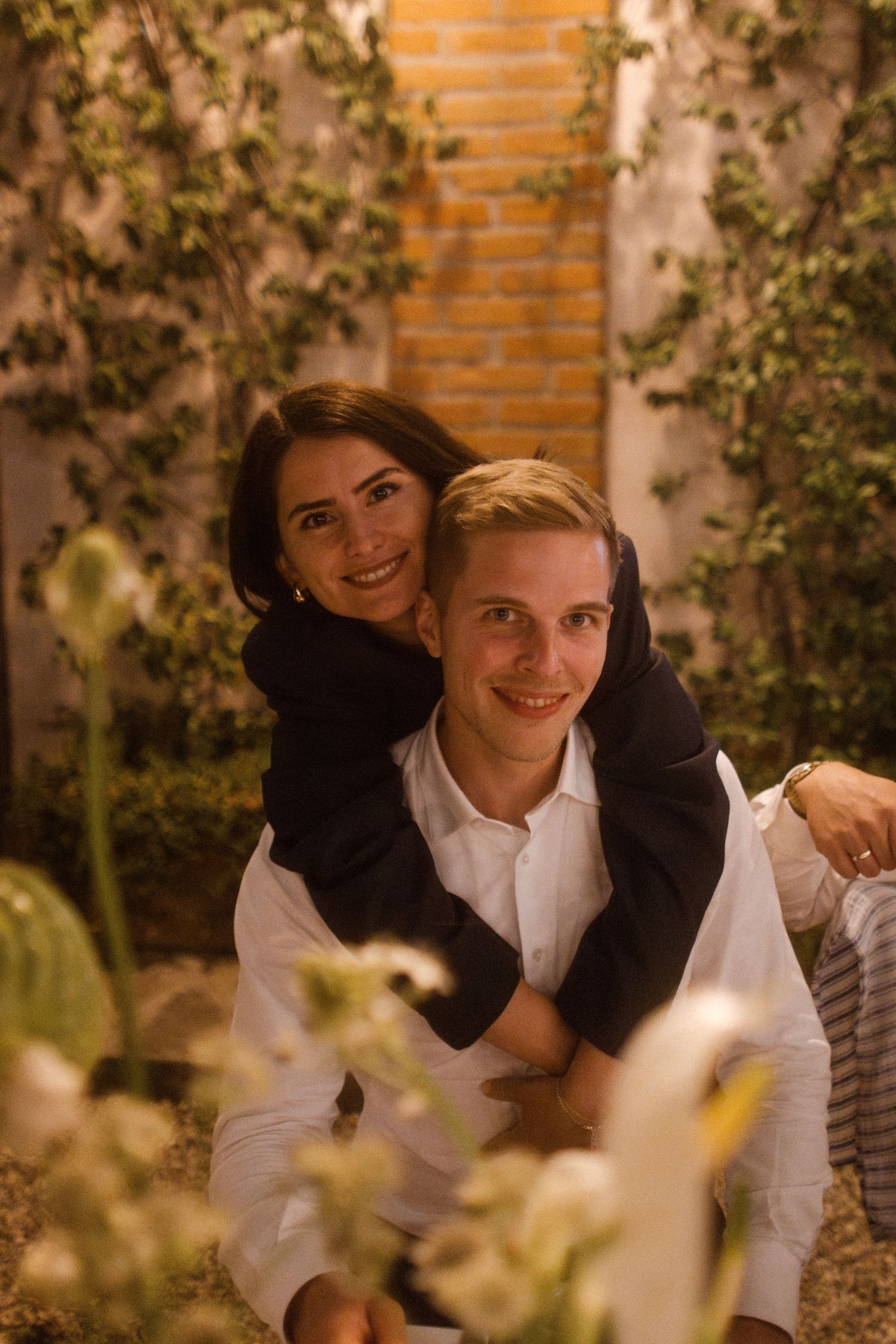Romantic evening portrait session in garden setting with brick wall and foliage.