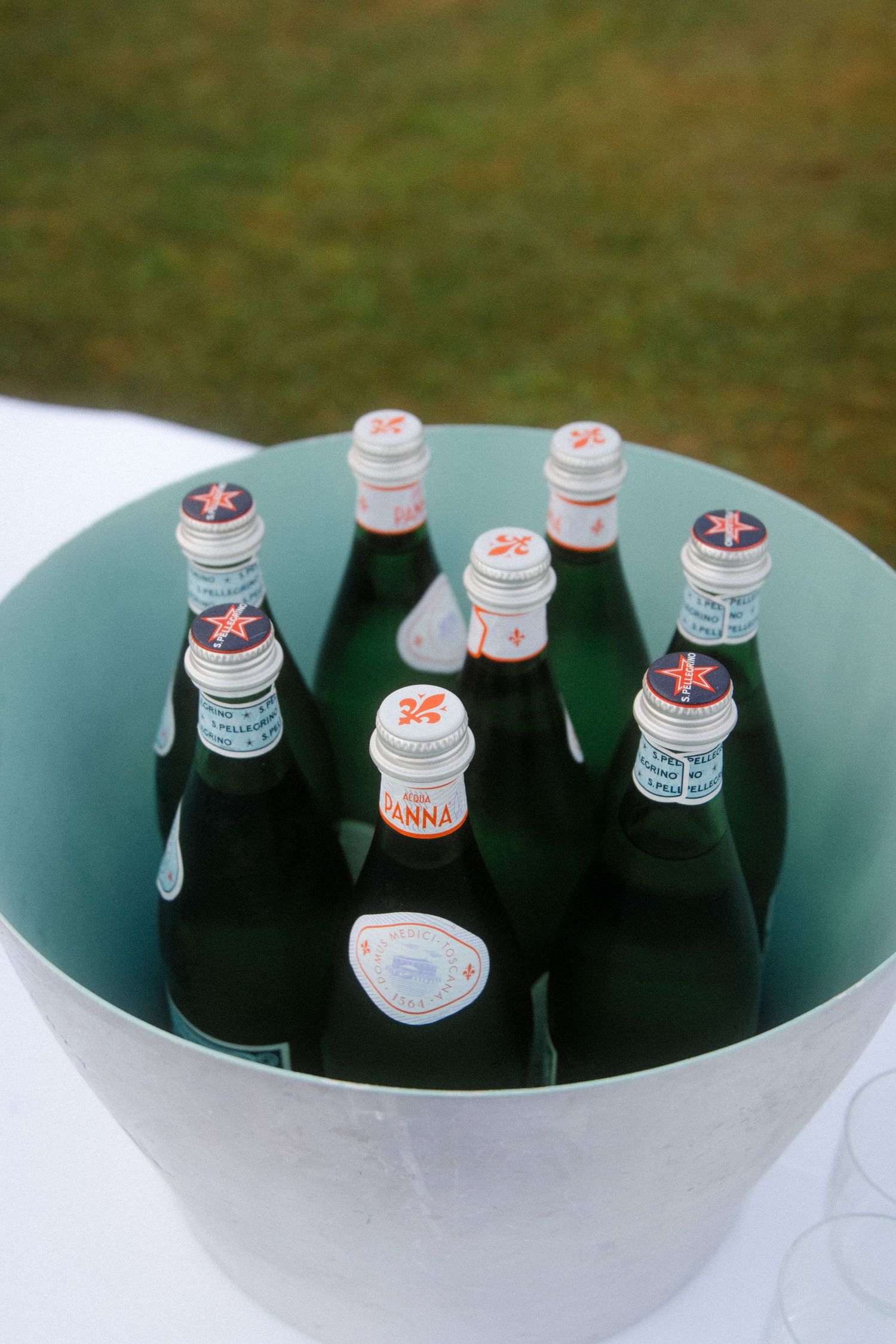 Glass bottles chilling in an ice bucket at an outdoor event.
