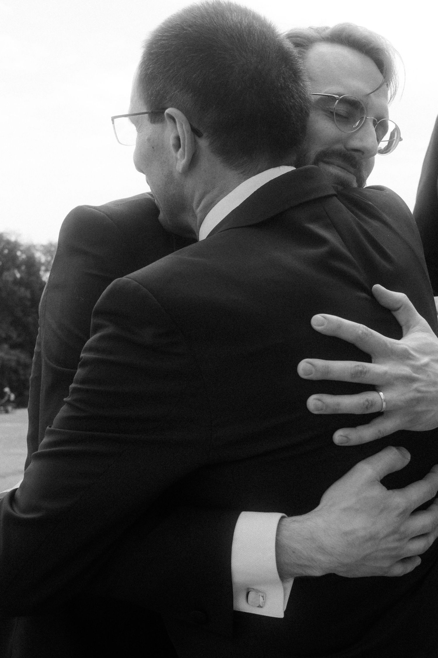 Black and white images of emotional embraces between wedding guests in formal attire.