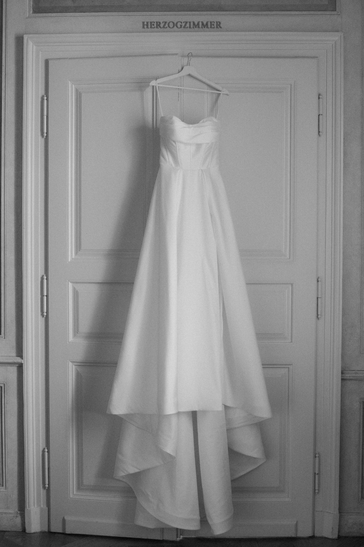 White wedding dress displayed on hangers against an elegant wall labeled Herzogzimmer.
