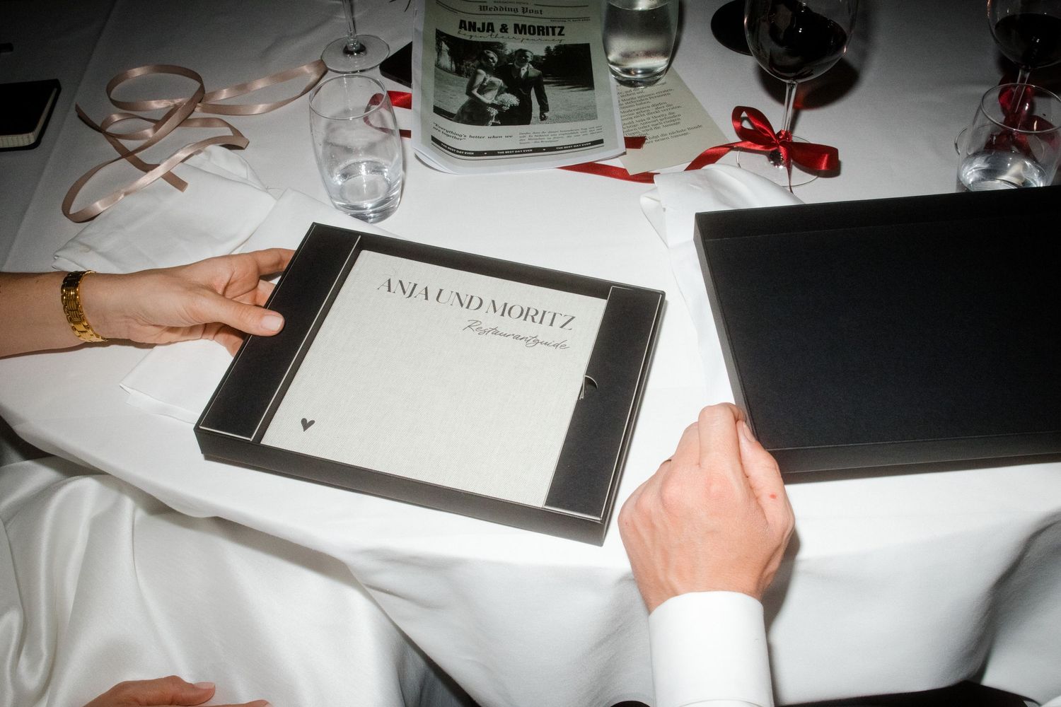 Hands holding an St. Moritz photography book at a formal white tablecloth dinner event.
