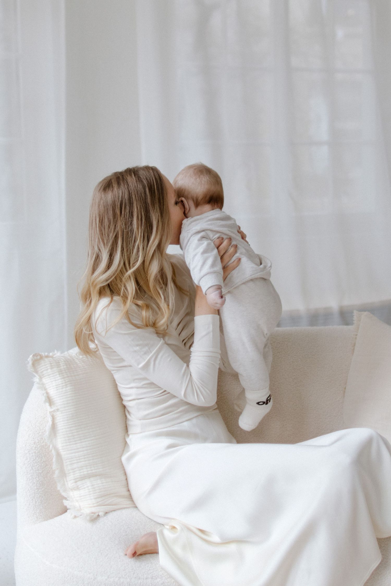 Mother and baby sharing tender moments on white couch with soft lighting.