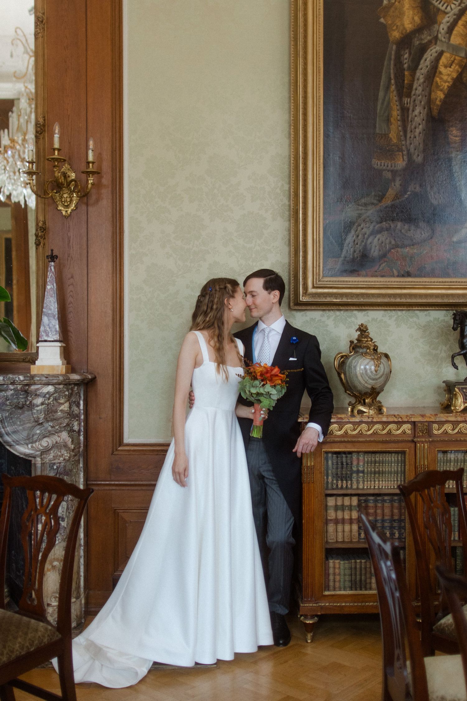 Wedding couple posing in an elegant room with antique furniture and classic artwork.