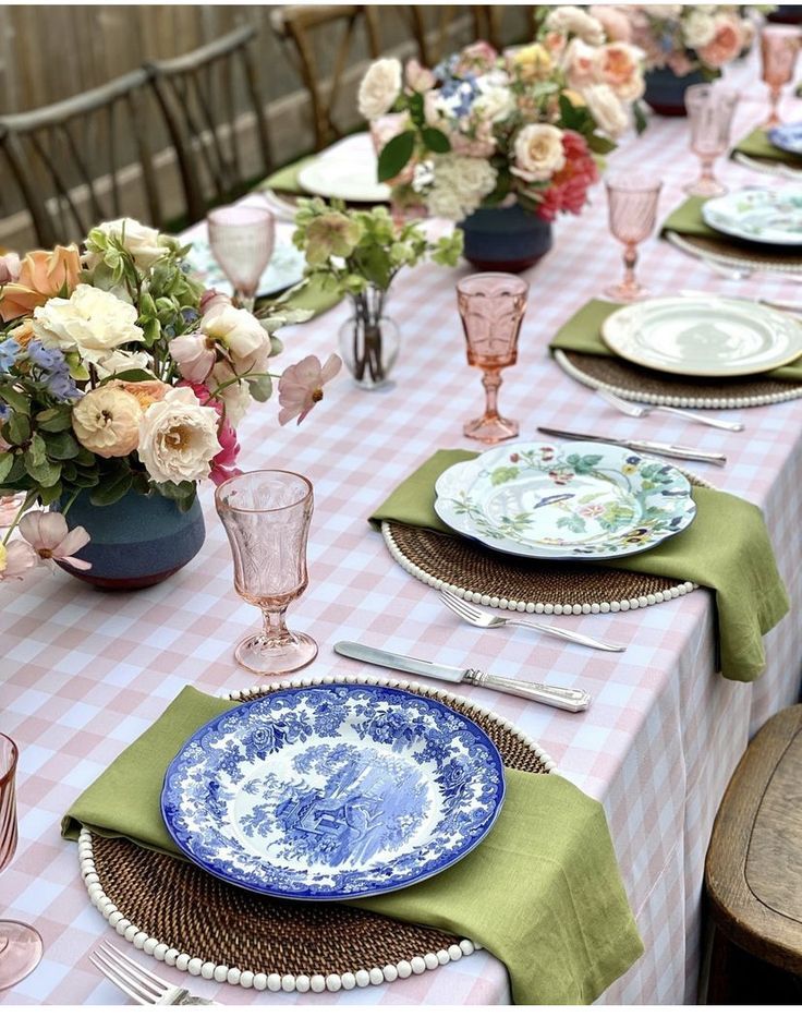 Table setting with blue and white china plates, pink glassware, and floral centerpieces.