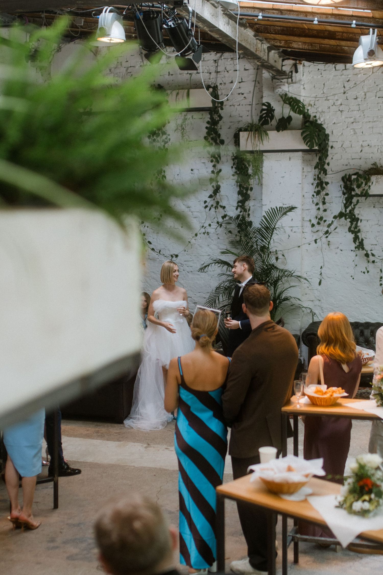 Wedding ceremony setup in an industrial space with white brick walls and hanging greenery.