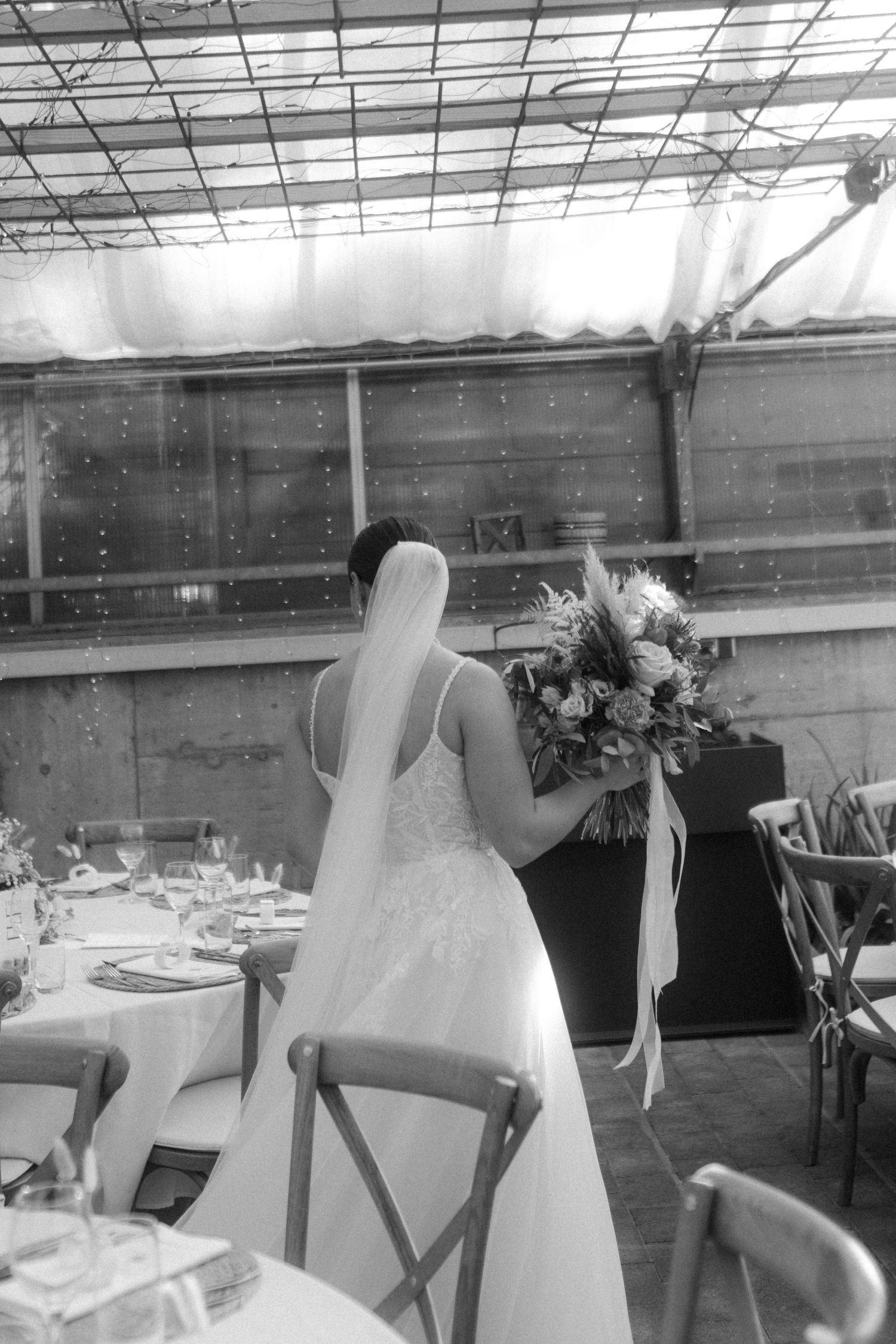 A black and white photo of a wedding reception setup in a greenhouse with floral arrangements.