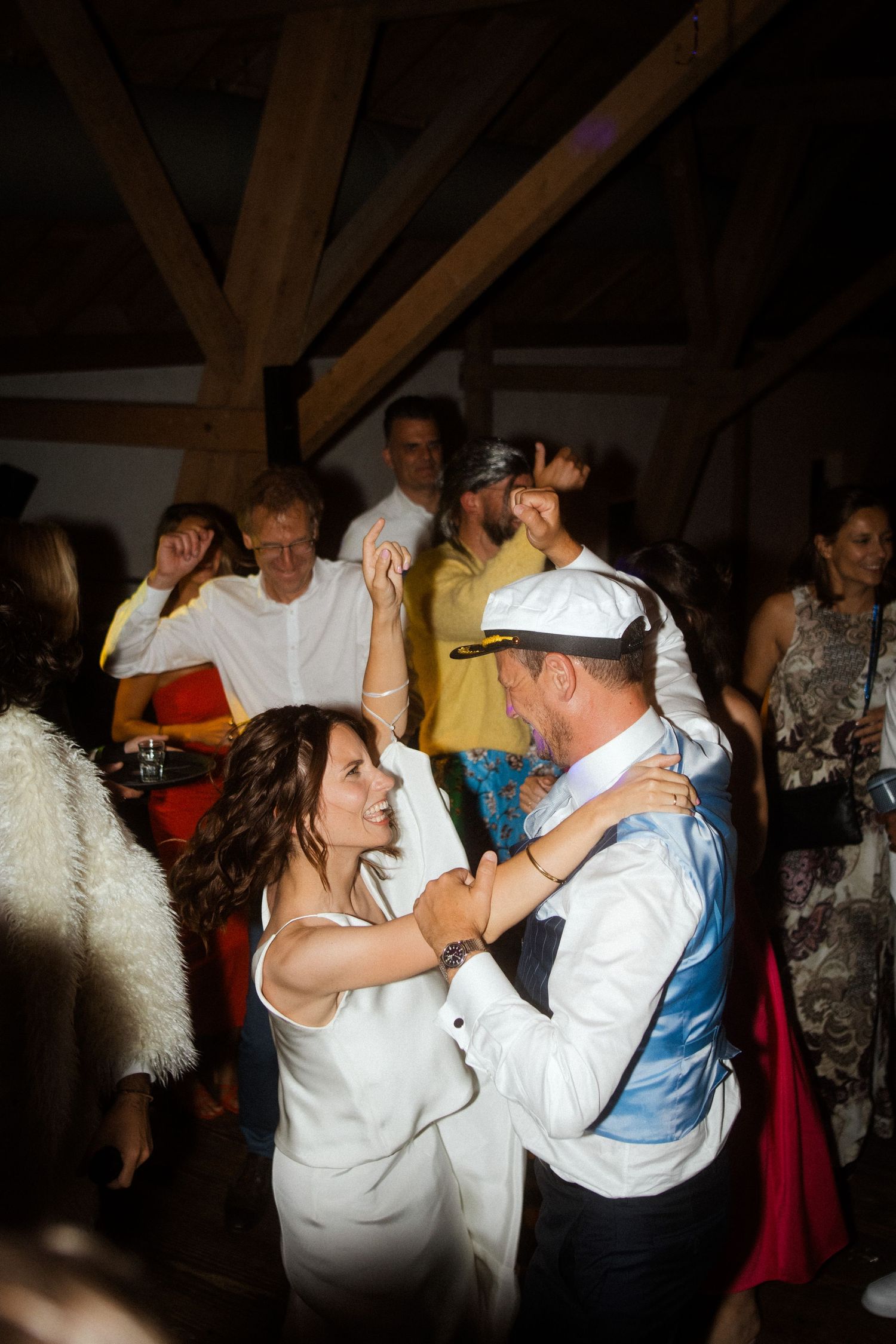 Couple dancing at wedding reception surrounded by guests under wooden beams.