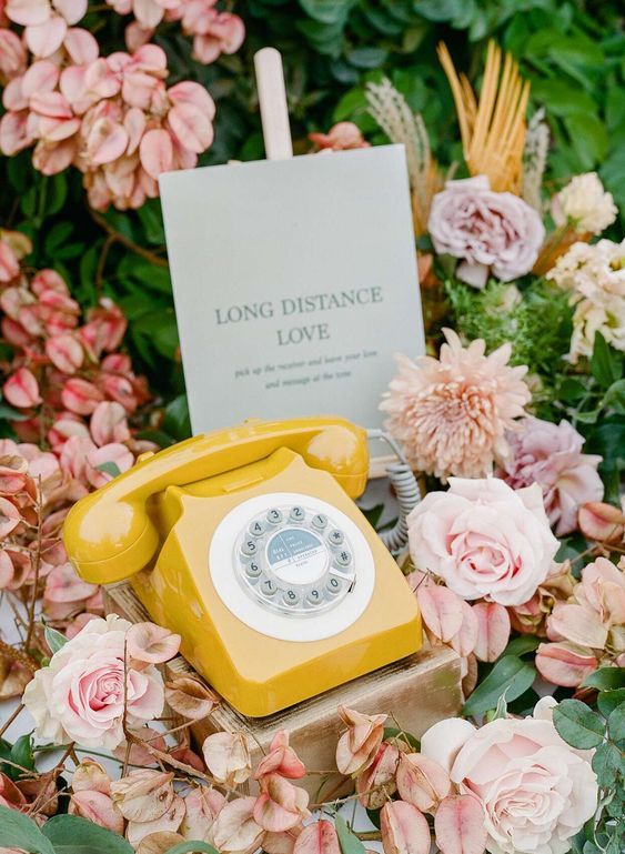 A vintage yellow rotary telephone surrounded by pink roses and a 'Long Distance Love' note card.