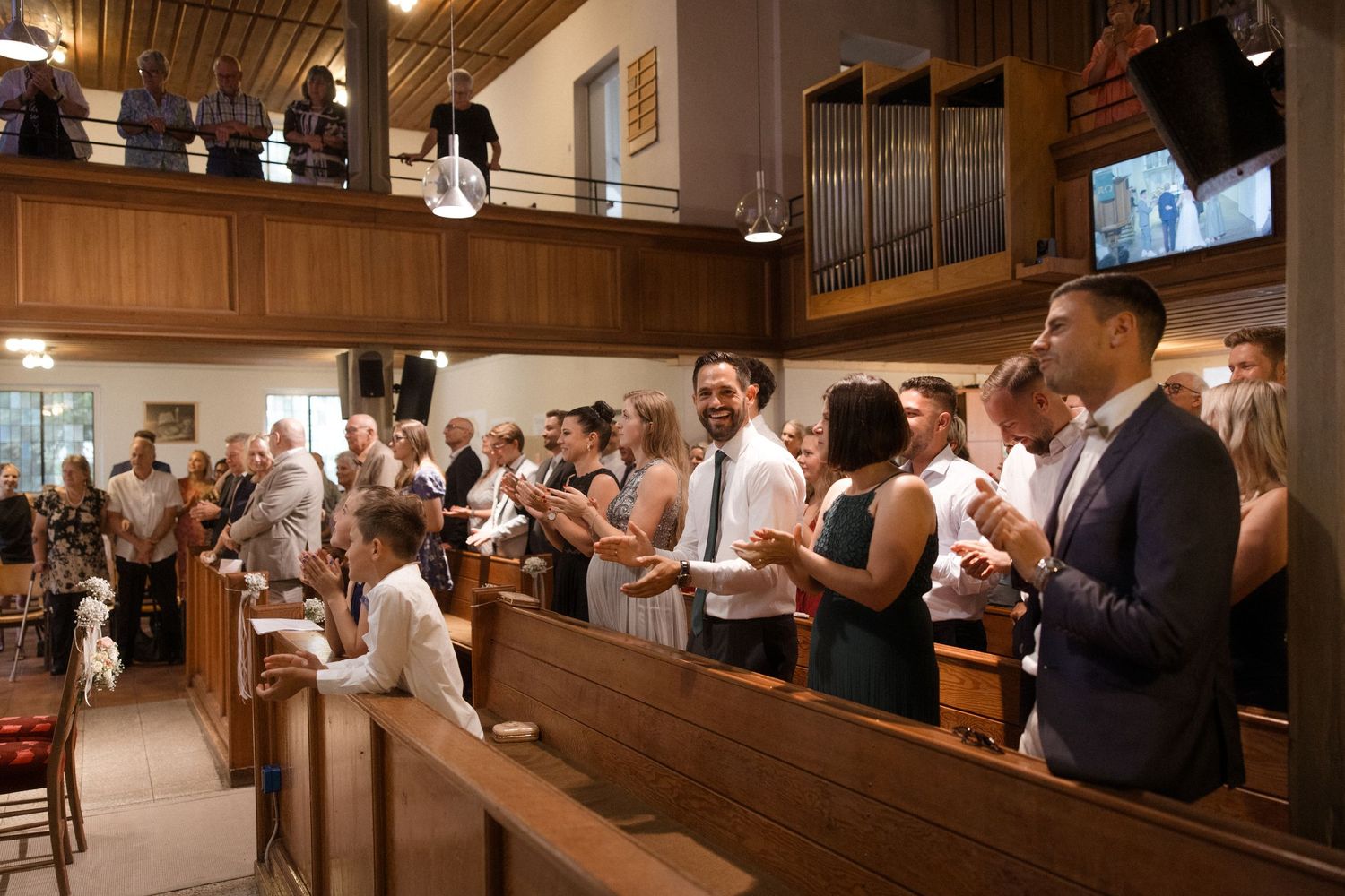 Wedding guests stand and applaud during ceremony in wood-paneled church.