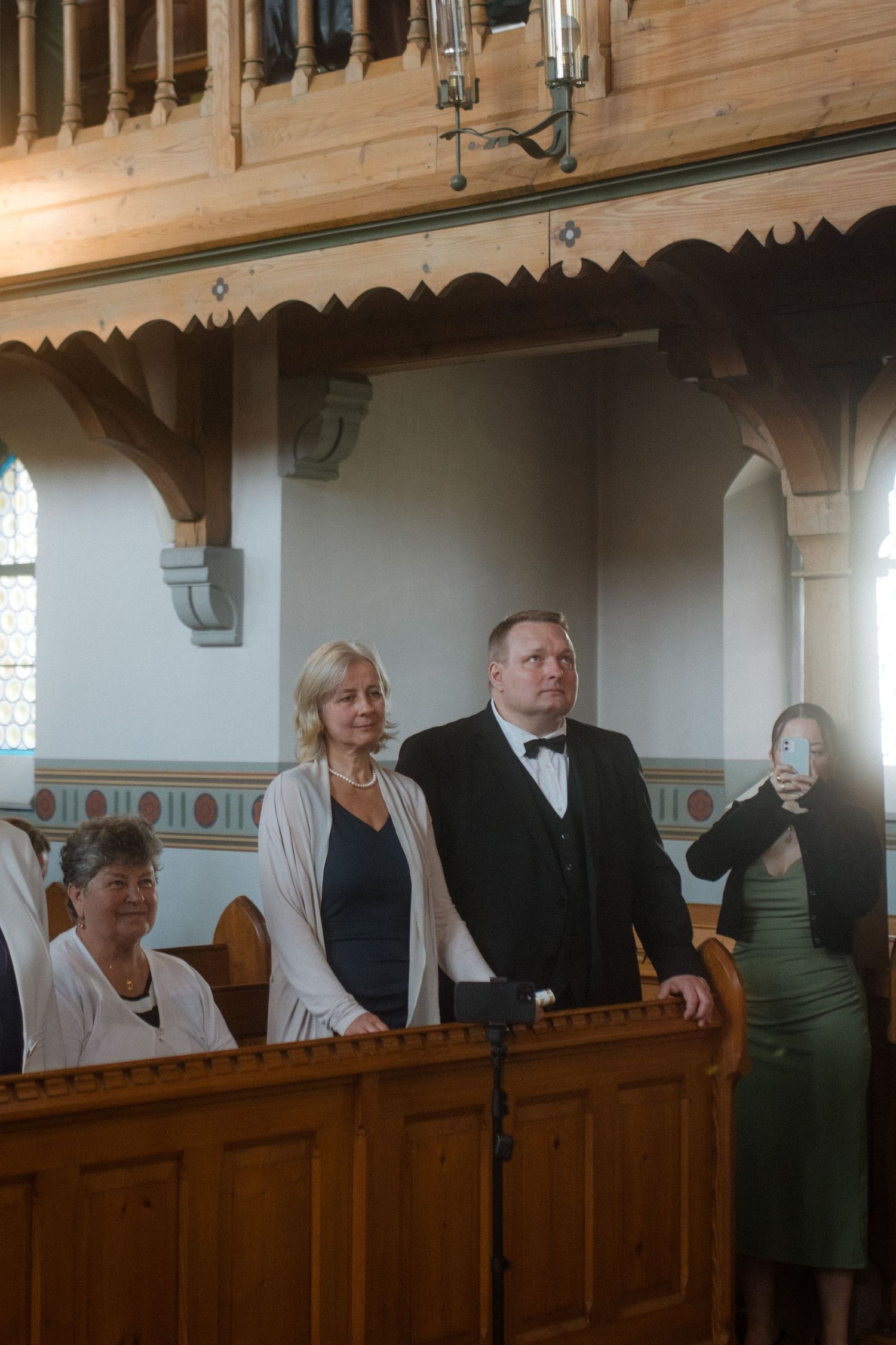 Wedding guests stand in wooden church pews during a ceremony.