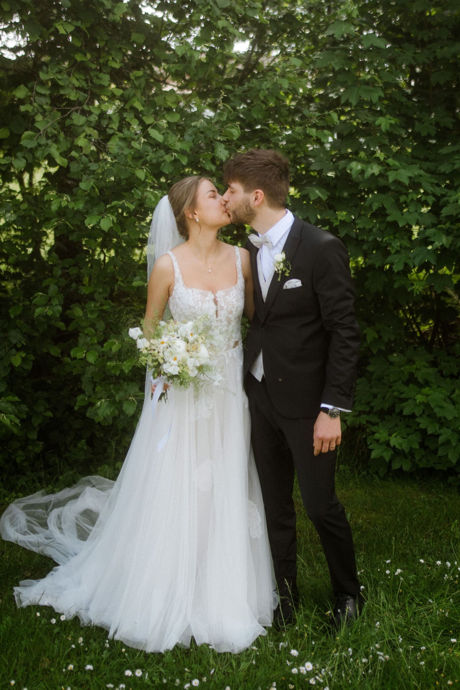 Romantic garden wedding portrait with couple sharing an intimate moment among green foliage.