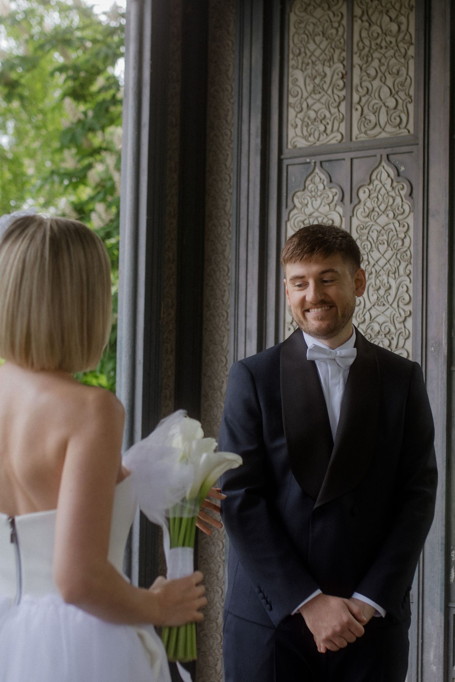Wedding couple shares a moment in front of an ornately decorated door panel.