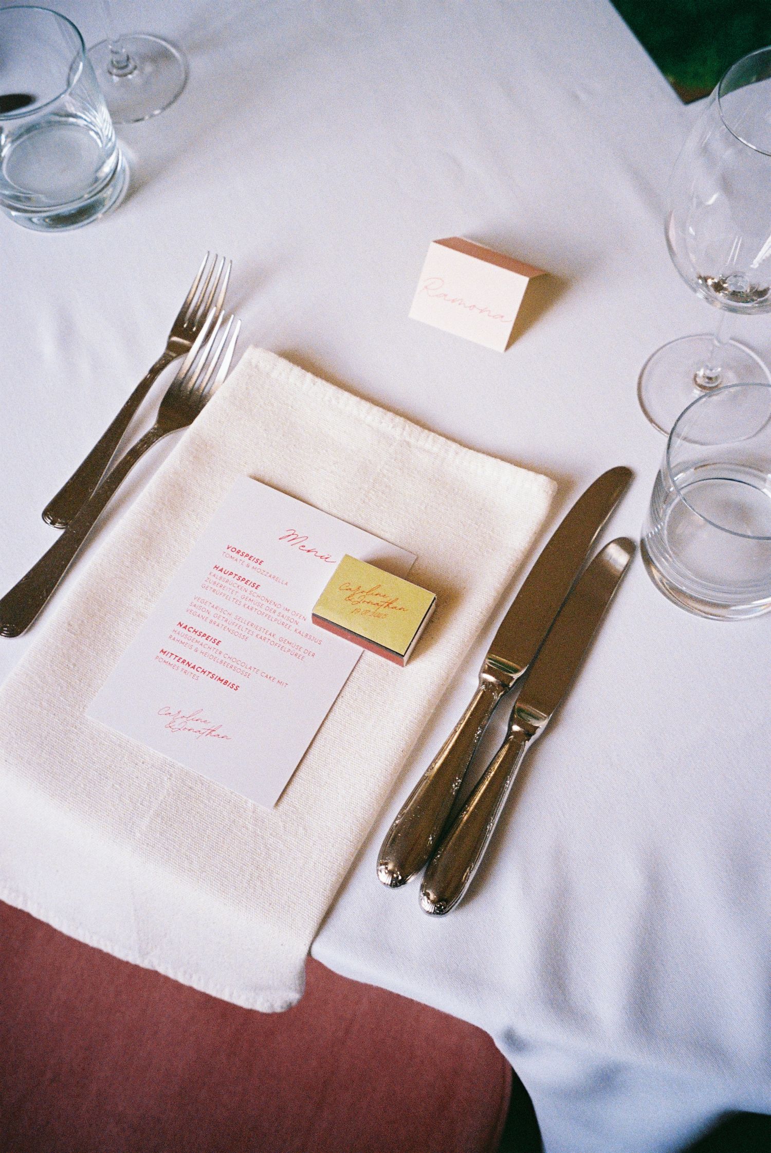 Elegant place setting with white napkin, silverware, menu card and wine glasses on crisp white tablecloth.