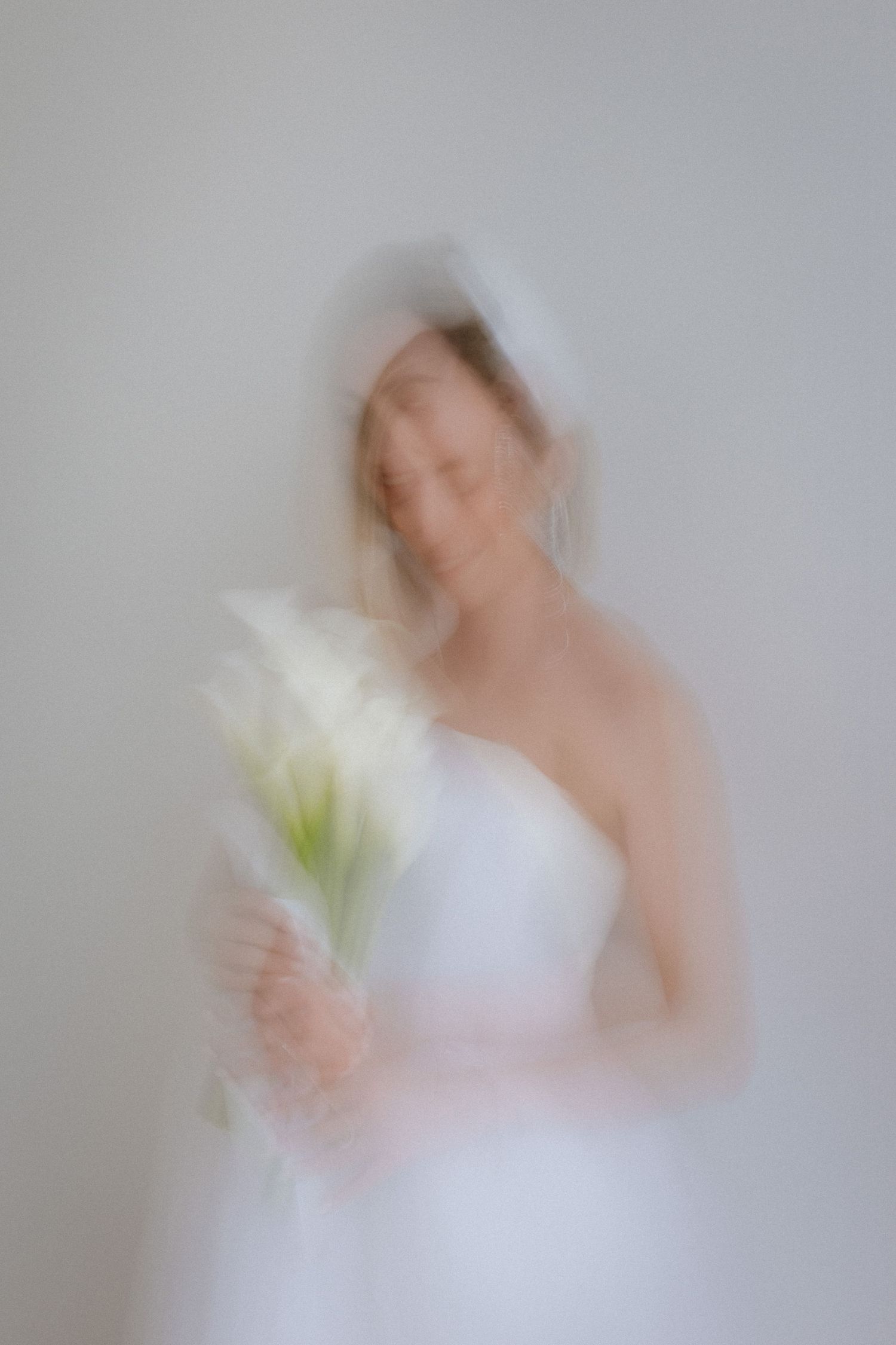 Artistic motion blur of person in white dress holding white flowers.