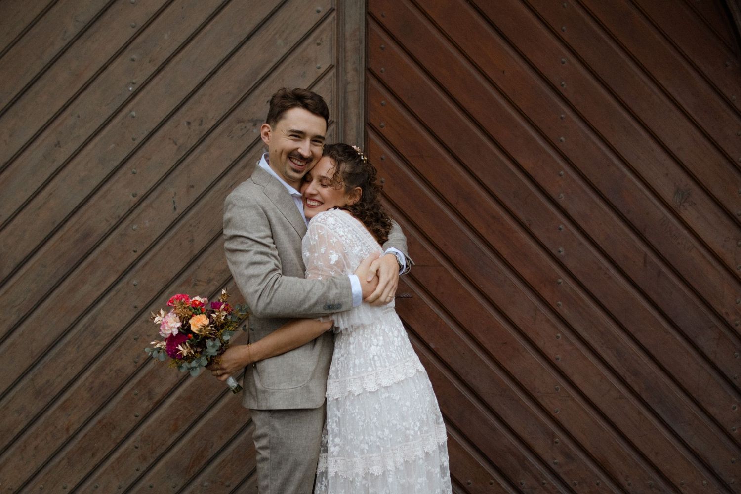Couple embracing against wooden wall background during wedding celebration.