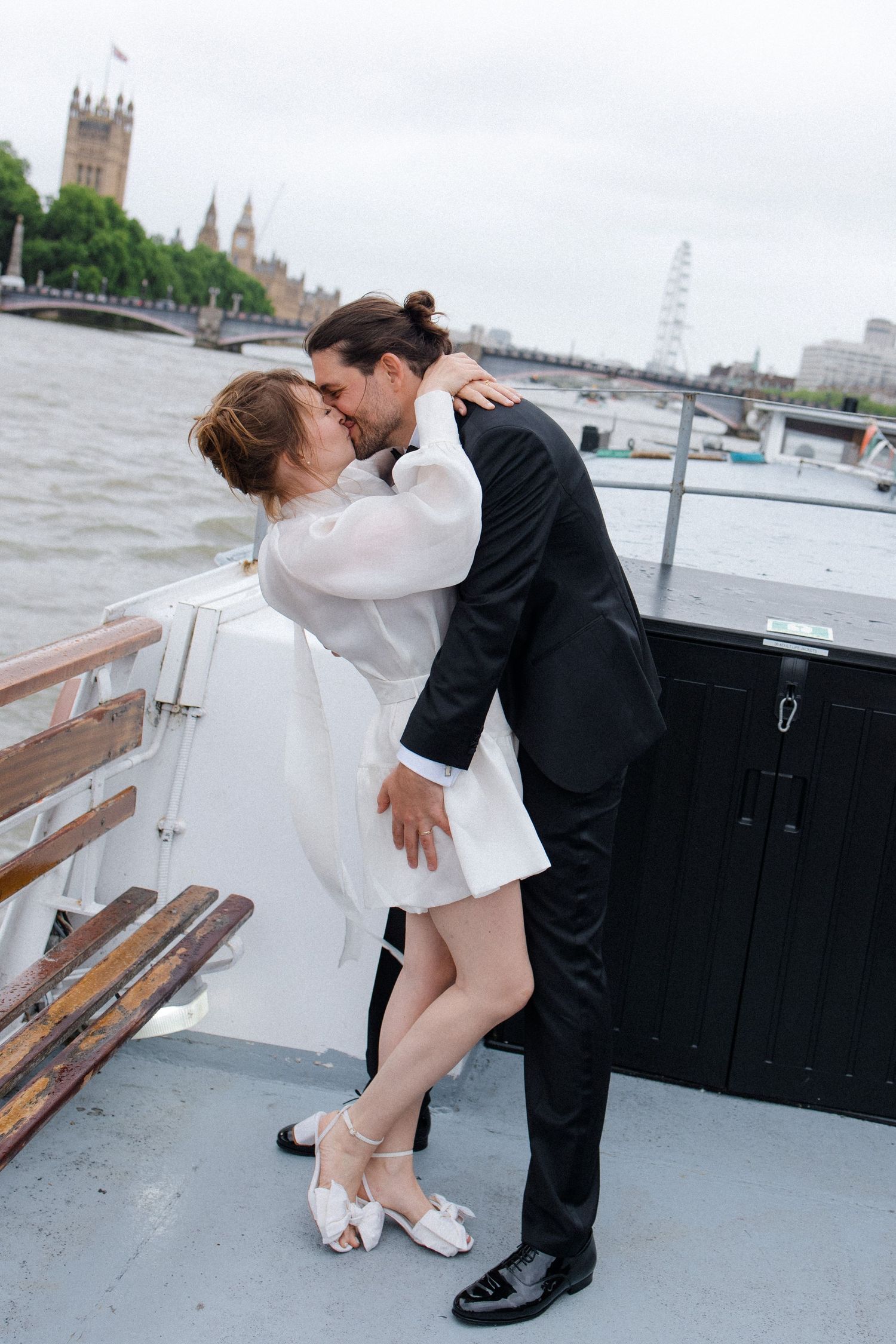 Couple kissing on a boat on the River Thames with the London Eye and Big Ben in the background.