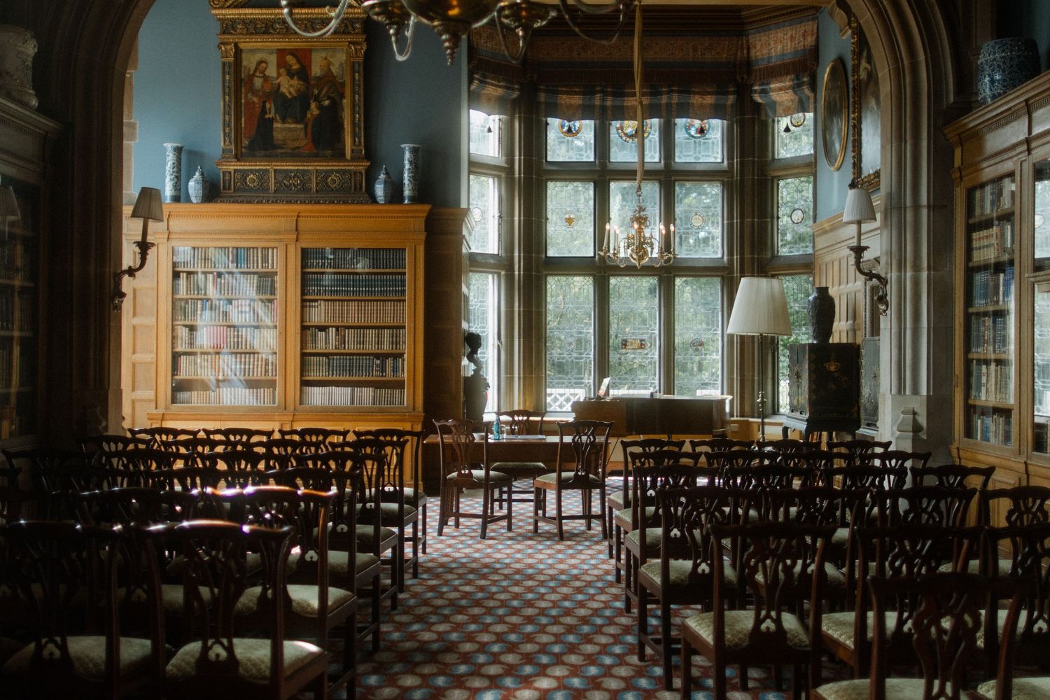 Historic library interior with bookshelves, large windows and chandeliers in panoramic view.