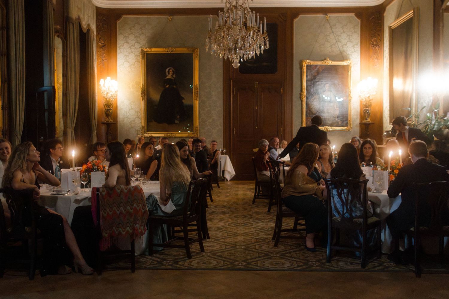 Elegant dining room with crystal chandelier and guests seated at tables for an evening event.
