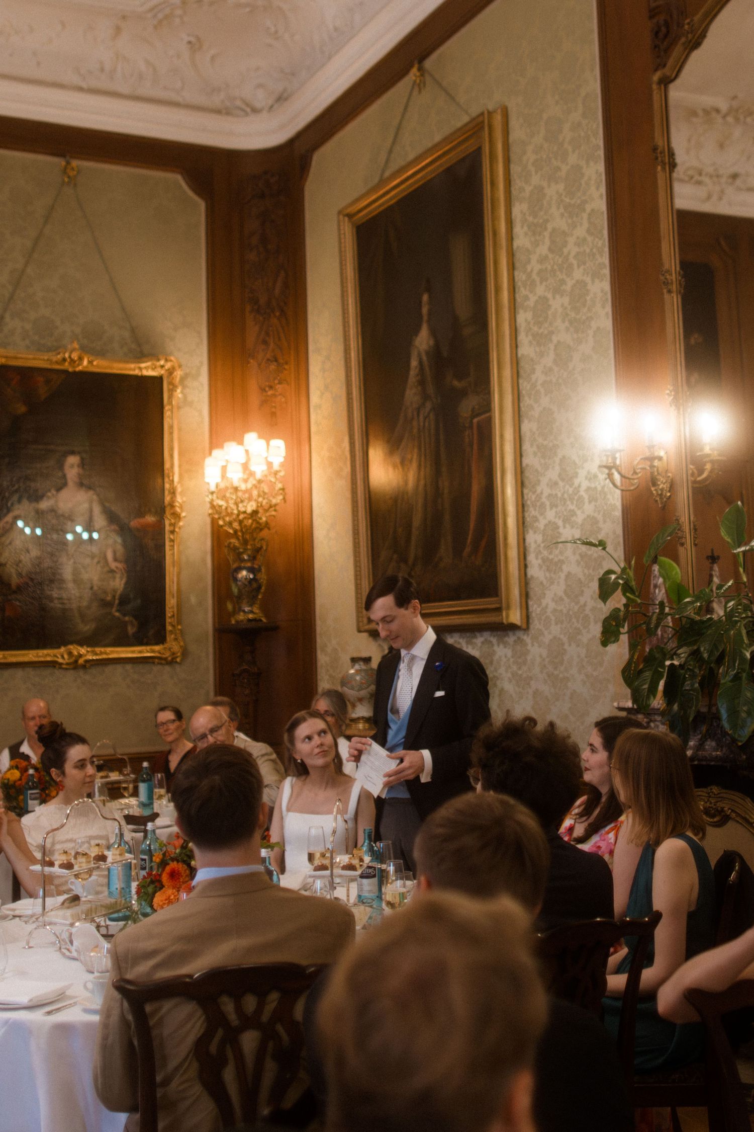 Elegant dining room with ornate gold-framed portraits and crystal chandeliers during an evening event.