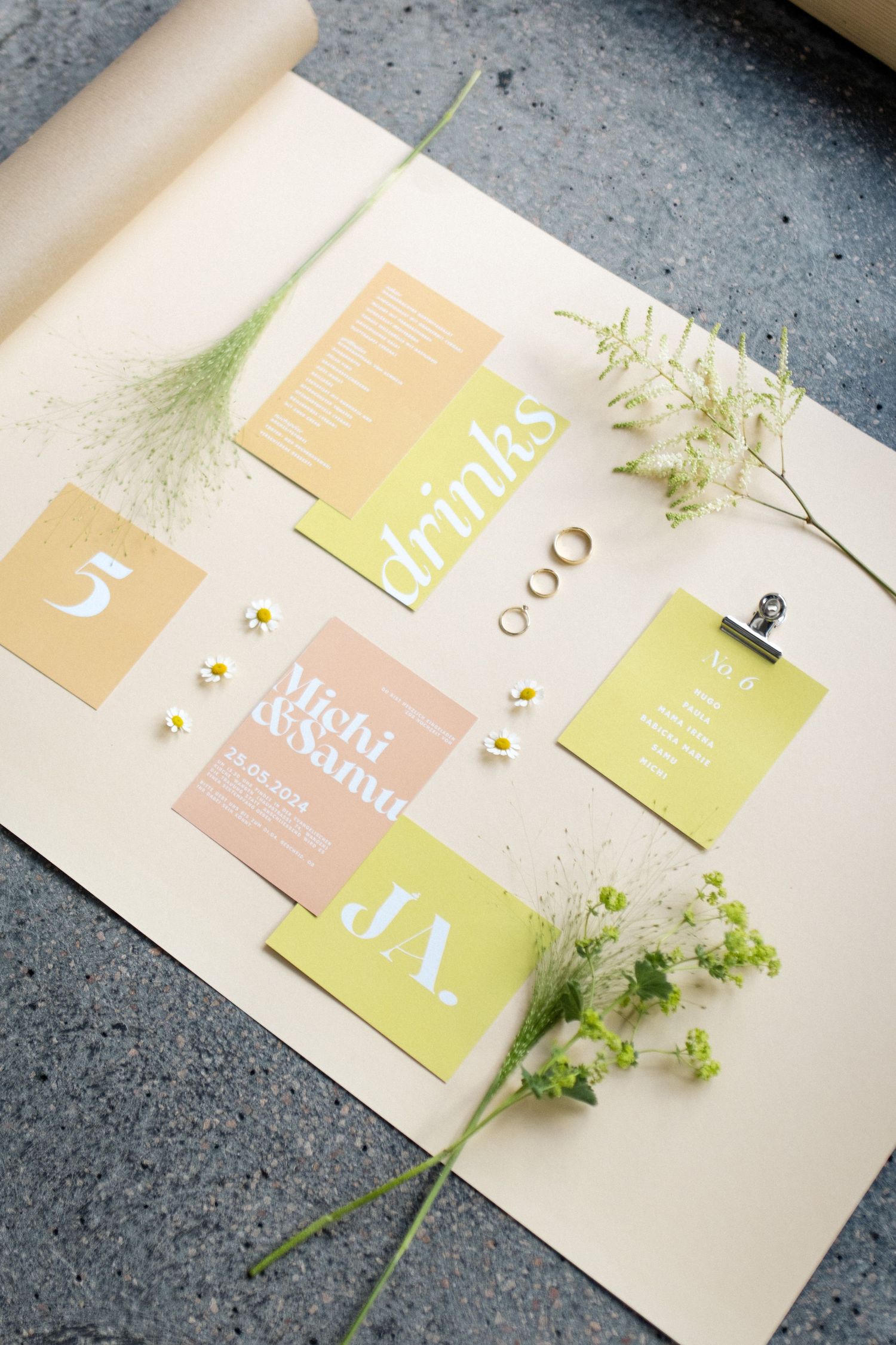 Wedding stationery layout with pale yellow and pink cards decorated with delicate white flowers and greenery.