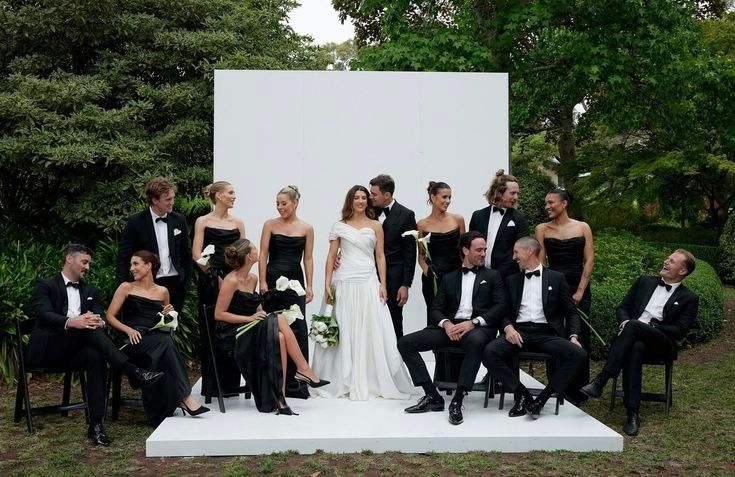 Wedding party arranged on white platform outdoors with bride and groom centered among attendants.