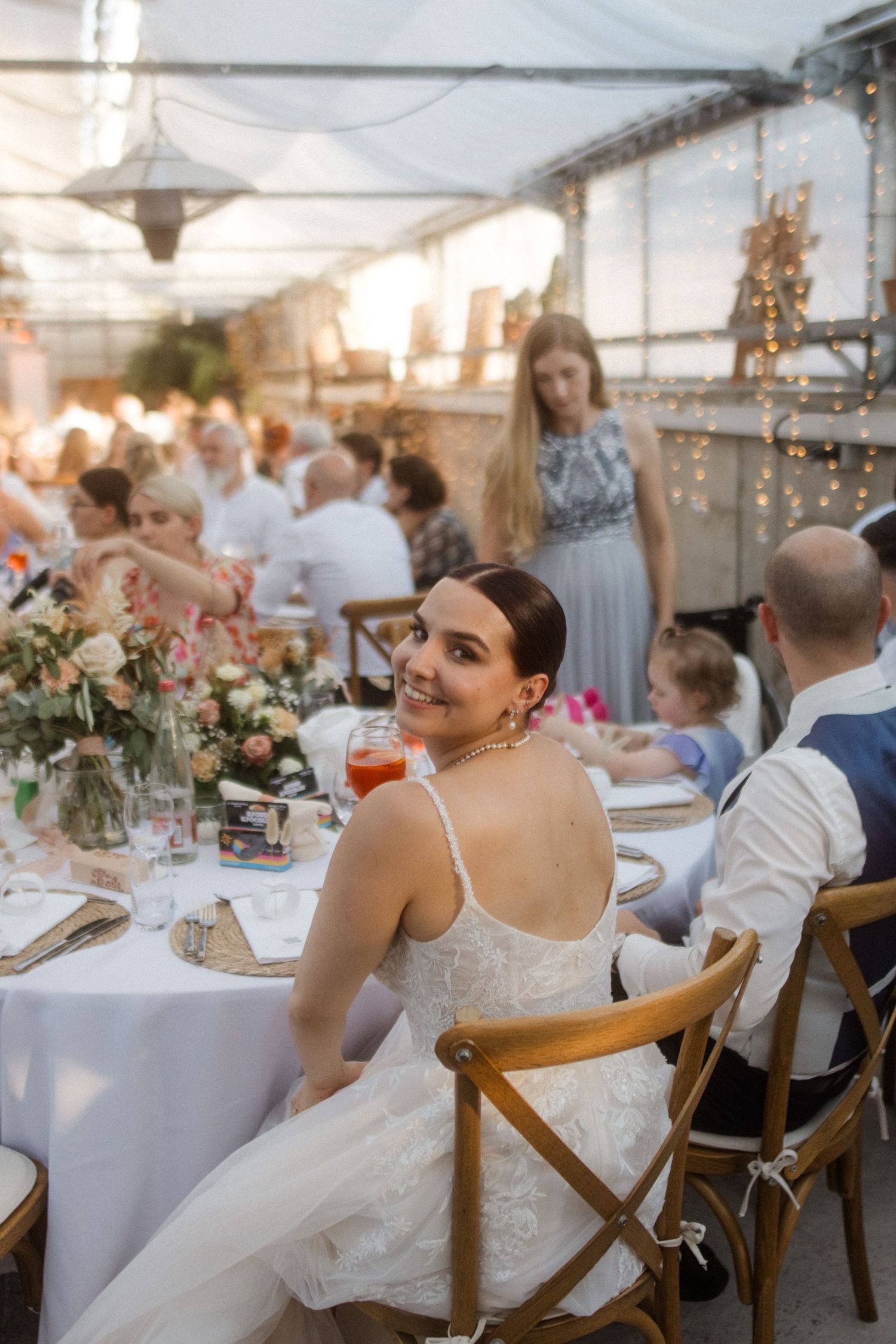 Reception dinner setup under a tent with string lights and elegant table settings.